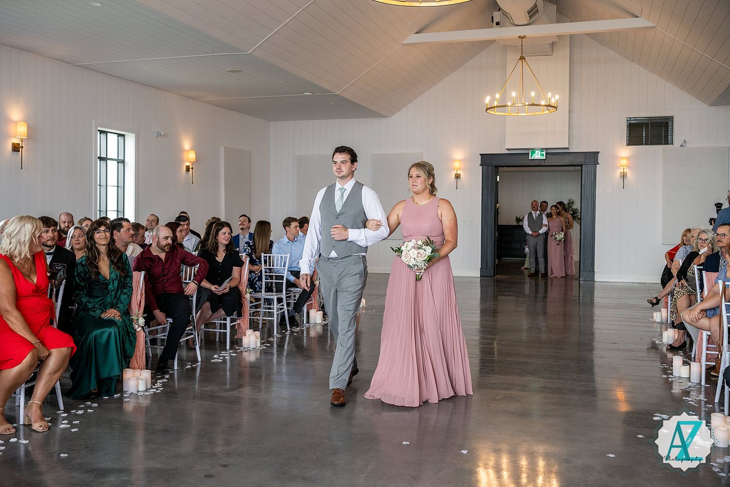 Wedding guests gather in a bright, elegant venue space with chandeliers and wall sconces.