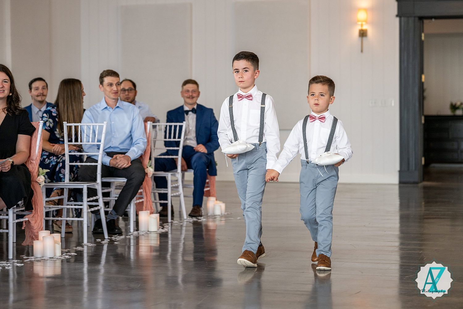 Wedding party members in formal attire including suspenders and bowties gather in an elegant light-filled venue.