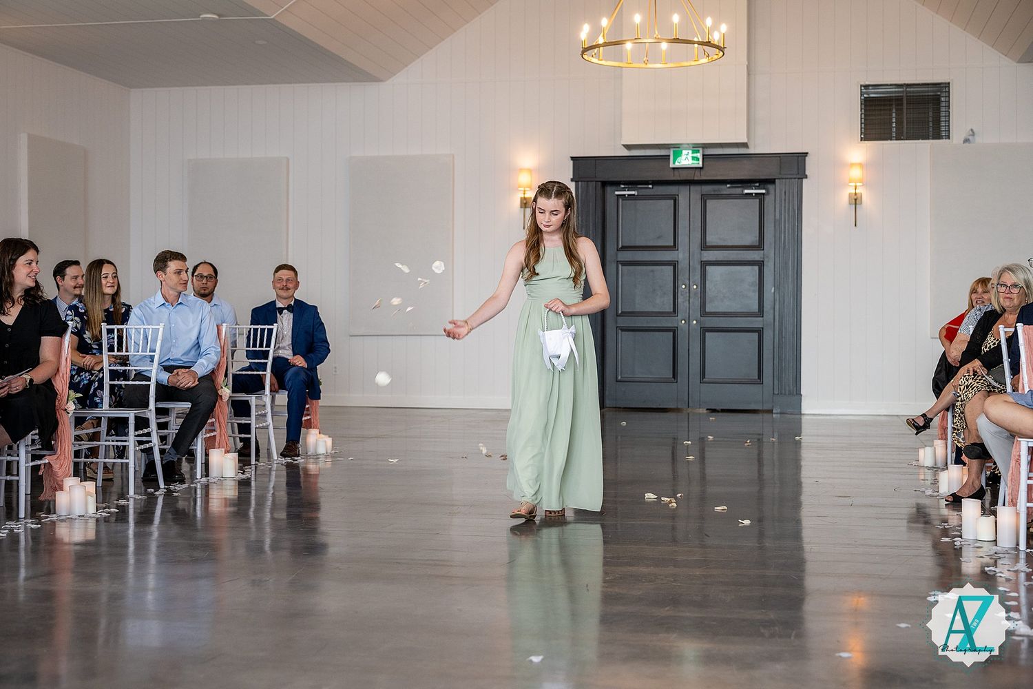 A bright wedding ceremony space features gray floors, white walls, and elegant chandeliers.