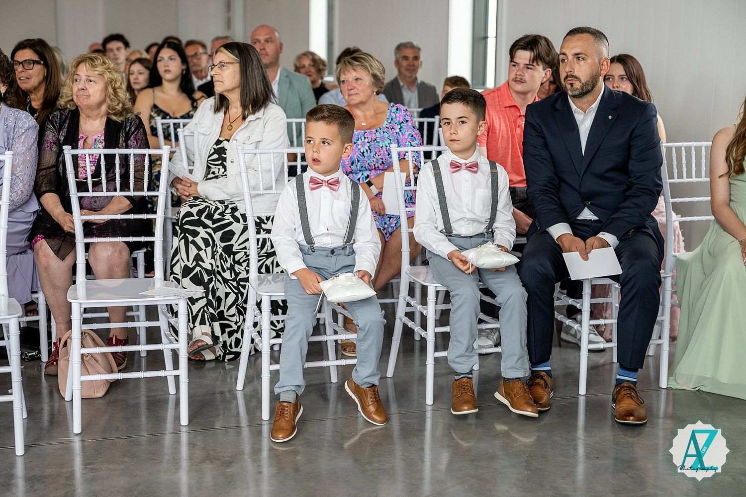 Wedding guests seated in white chairs along both sides of an indoor ceremony aisle.