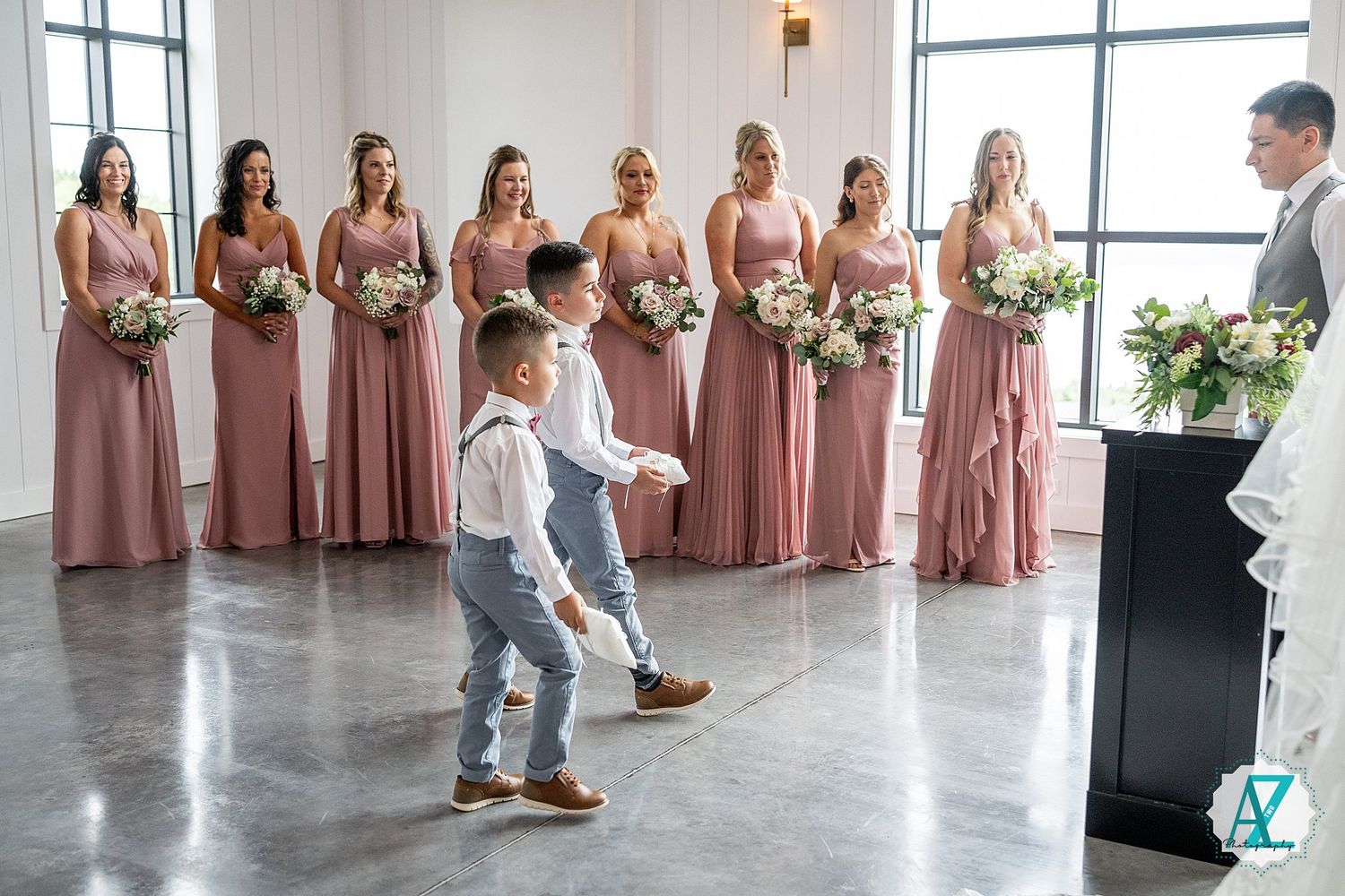 Elegant wedding party members stand in a line wearing coordinated pink and blue attire in a bright venue.