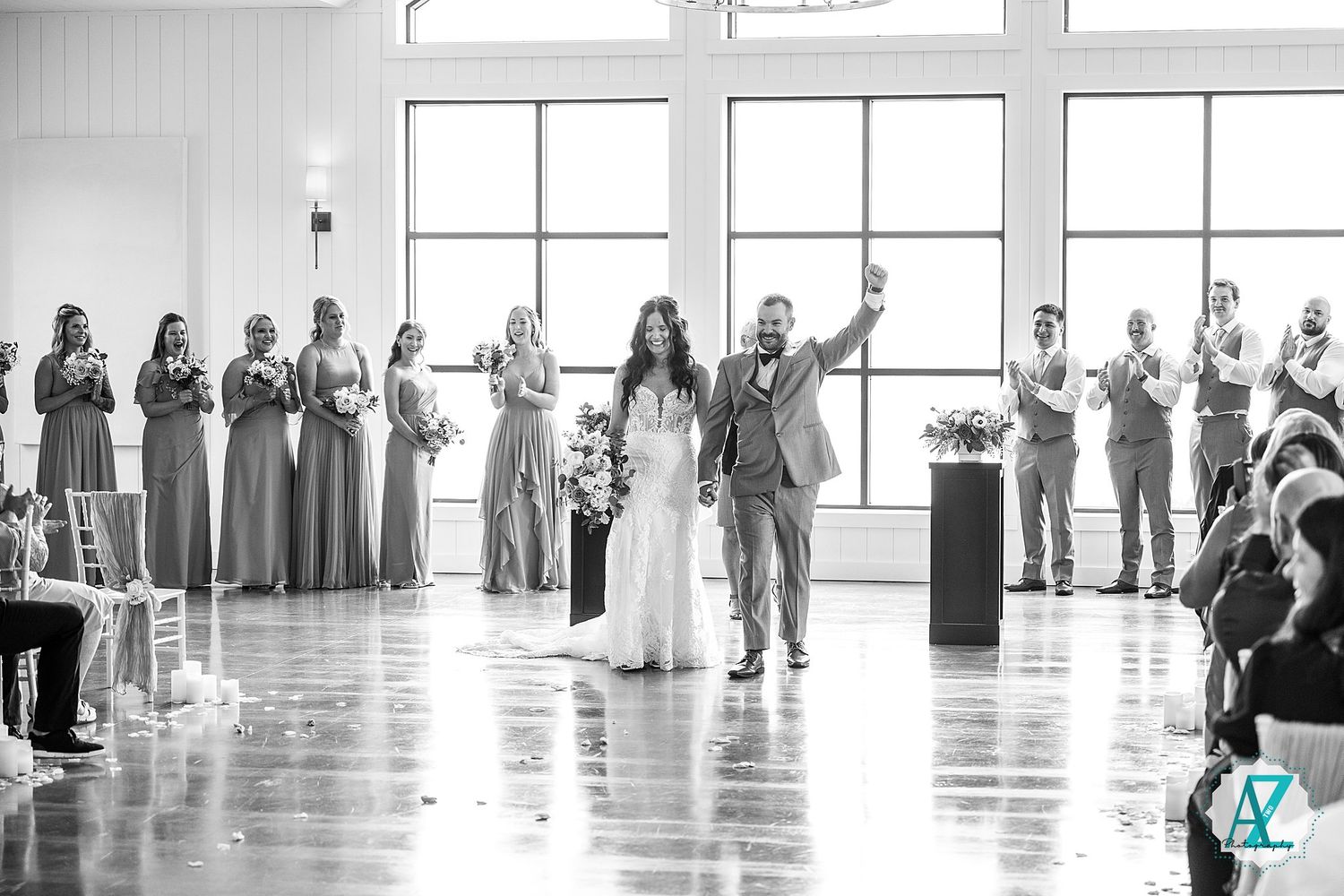 Black and white photo of wedding guests standing in a bright, window-lit room with white walls.