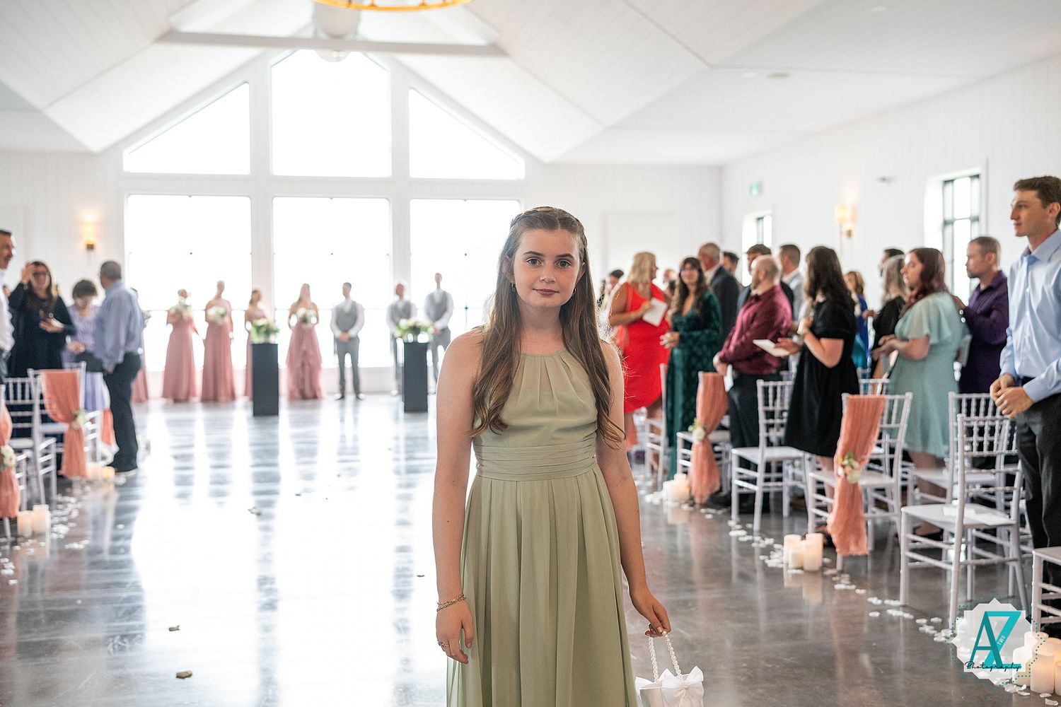 A wedding ceremony at a bright modern venue with bridesmaids in sage green dresses and guests in formal attire.