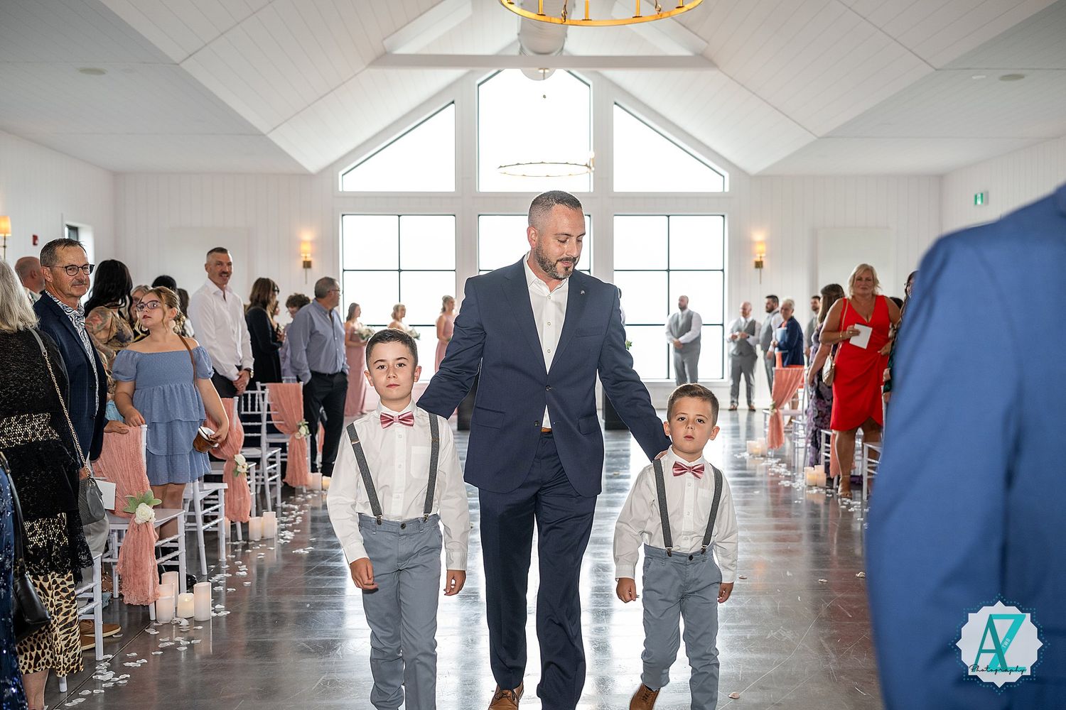 Wedding attendees gather in a bright indoor venue with white walls and windows during a celebratory reception event.