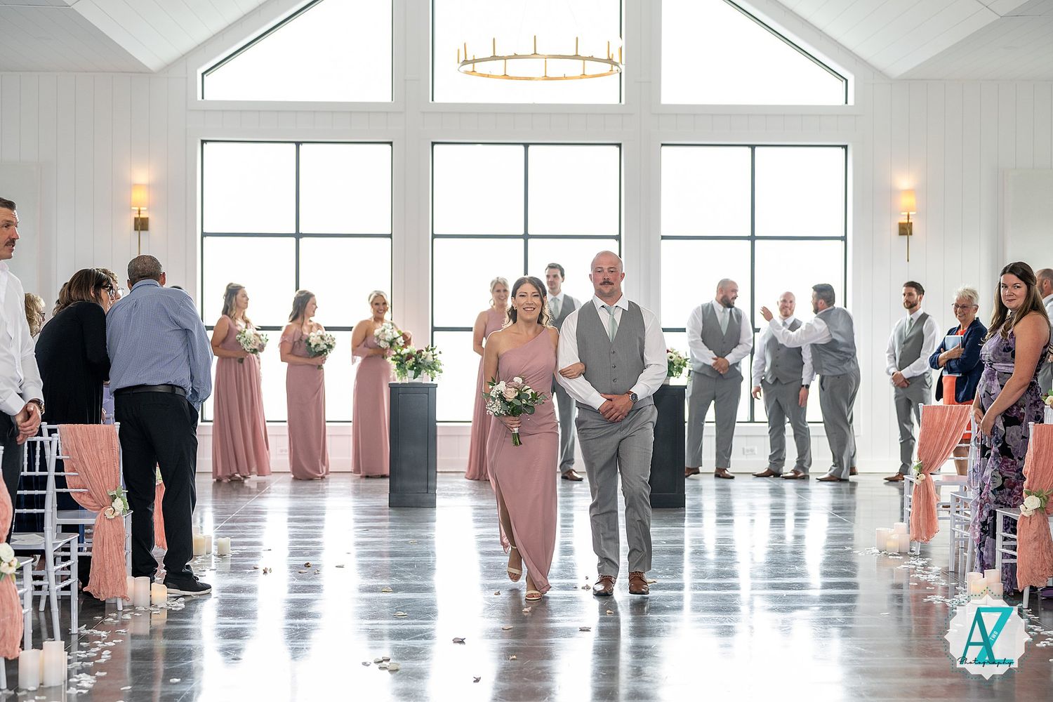 Wedding party poses in an elegant white room with large windows, forming a sequence of group photos along a wall.
