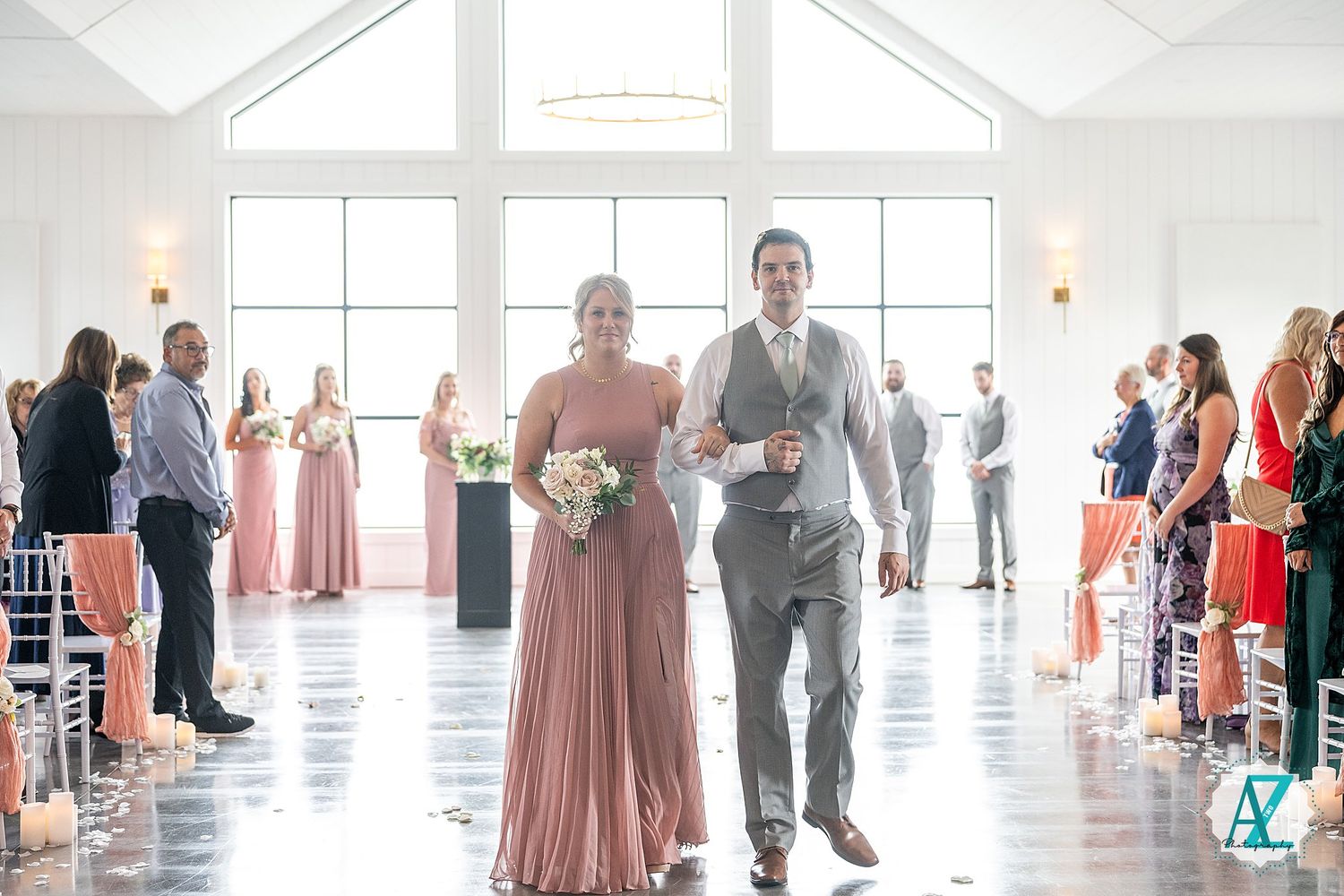Wedding guests line up inside a bright modern venue with high ceilings and large windows.