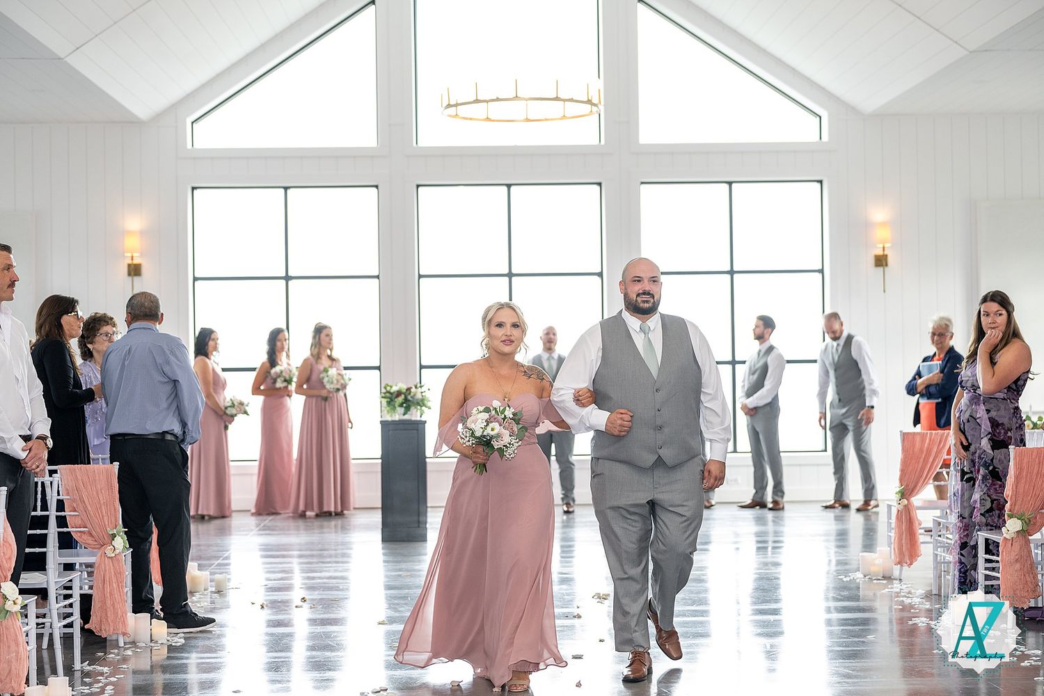 Wedding celebration in a grand white room with natural light streaming through large windows and people gathered.