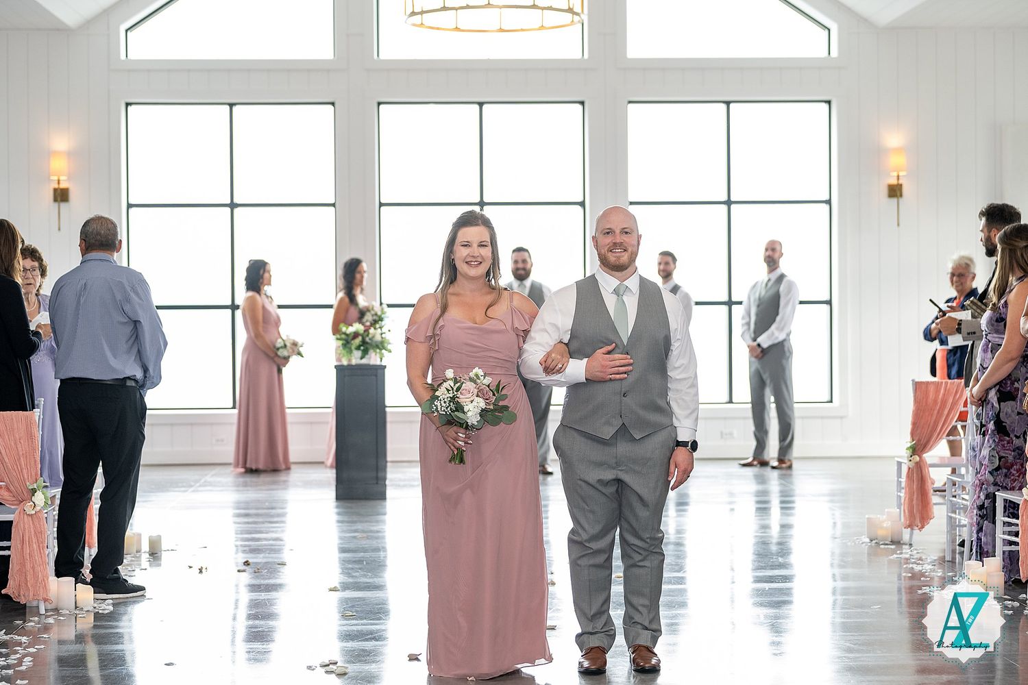 Elegant white wedding venue features floor-to-ceiling windows, crystal chandeliers, and guests in formal attire.
