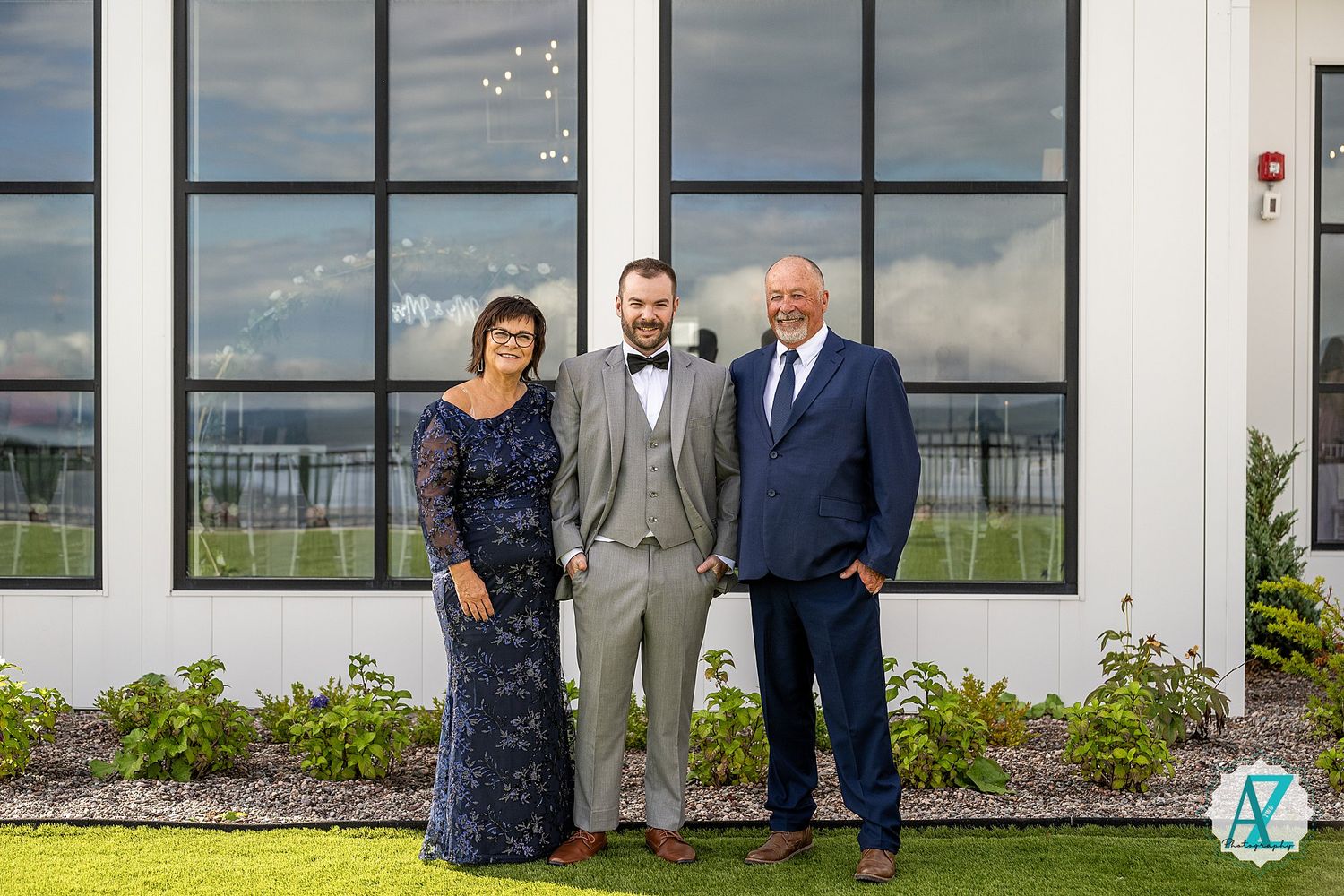 Wedding celebration group standing outside white modern venue with industrial windows and overcast sky.