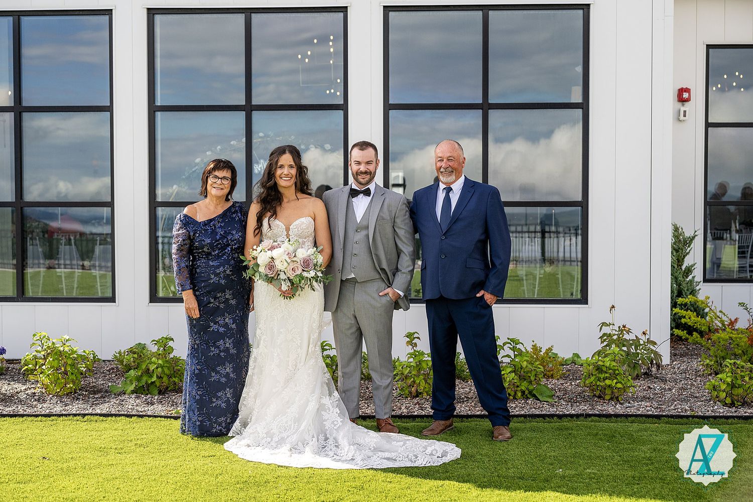Wedding party gathered outside modern white building with large black-framed windows.