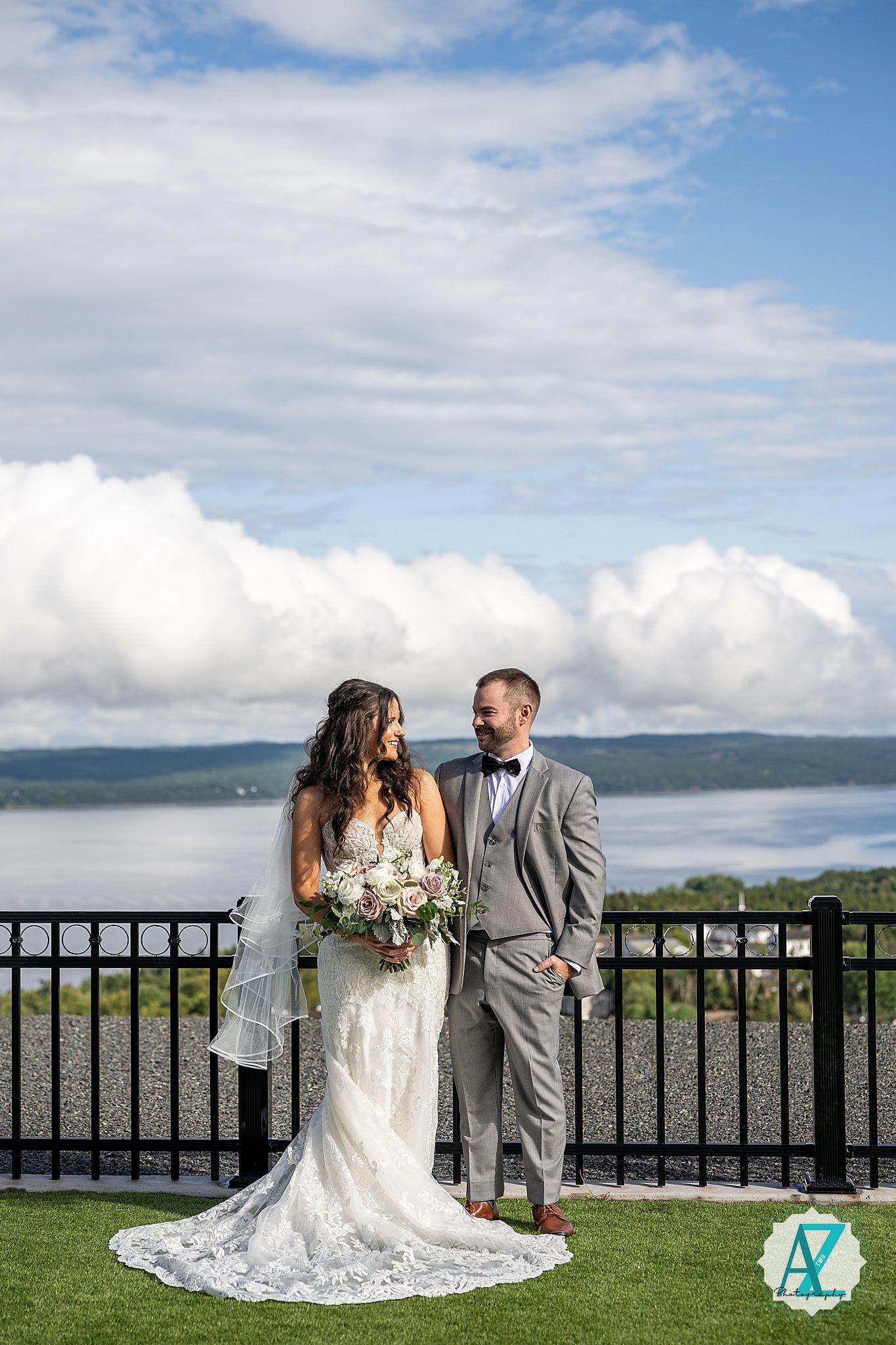 Wedding couple poses romantically by black railing with scenic mountain and lake views in background.