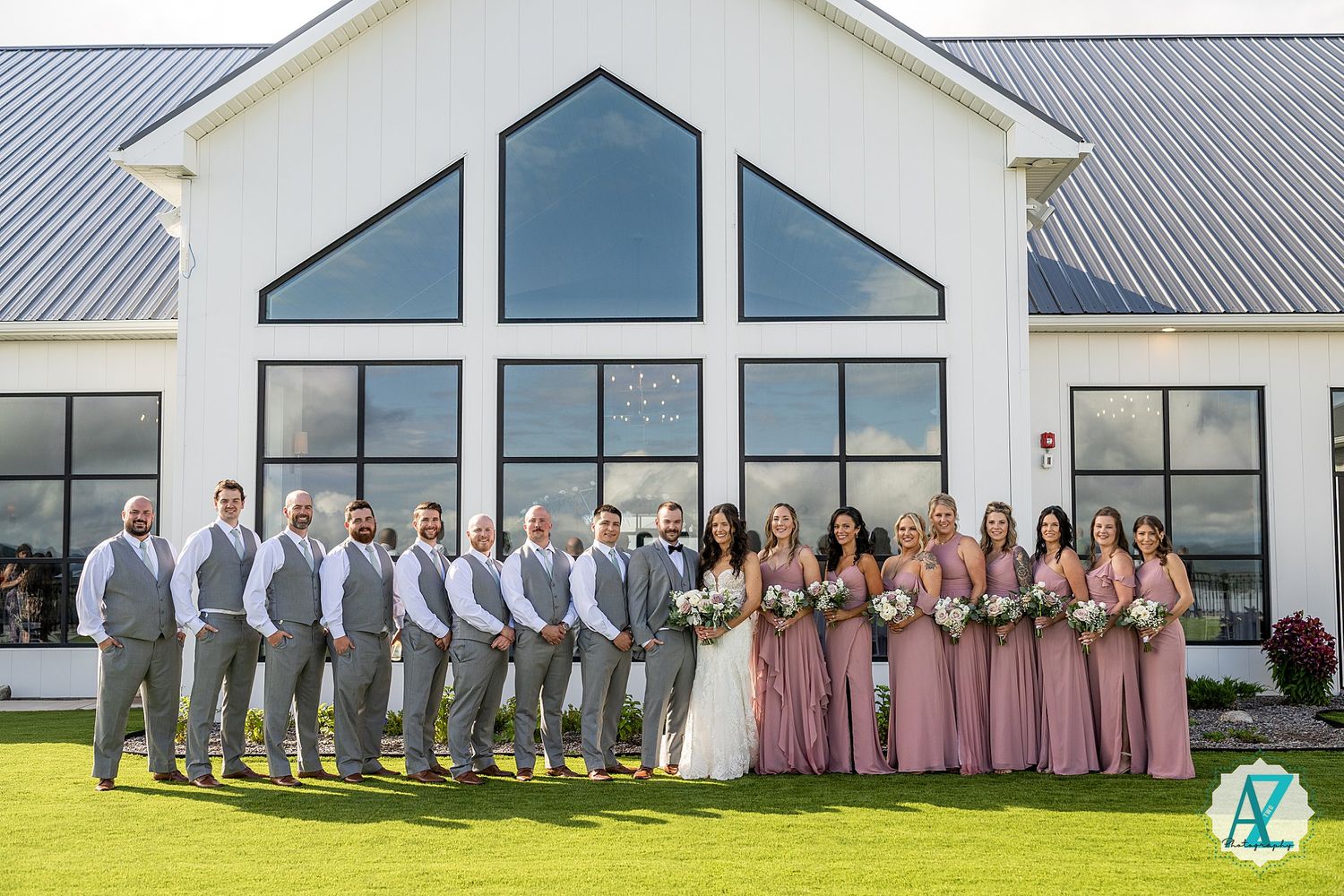 Wedding party wearing pink dresses and gray suits lines up against modern white building exterior.