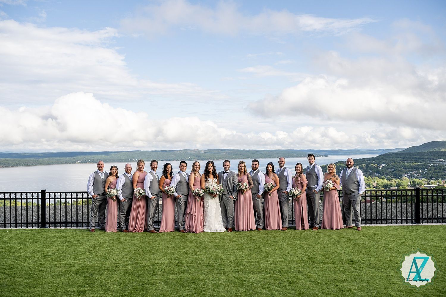 Wedding party lined up on a scenic hilltop with mountains and blue sky in the background.