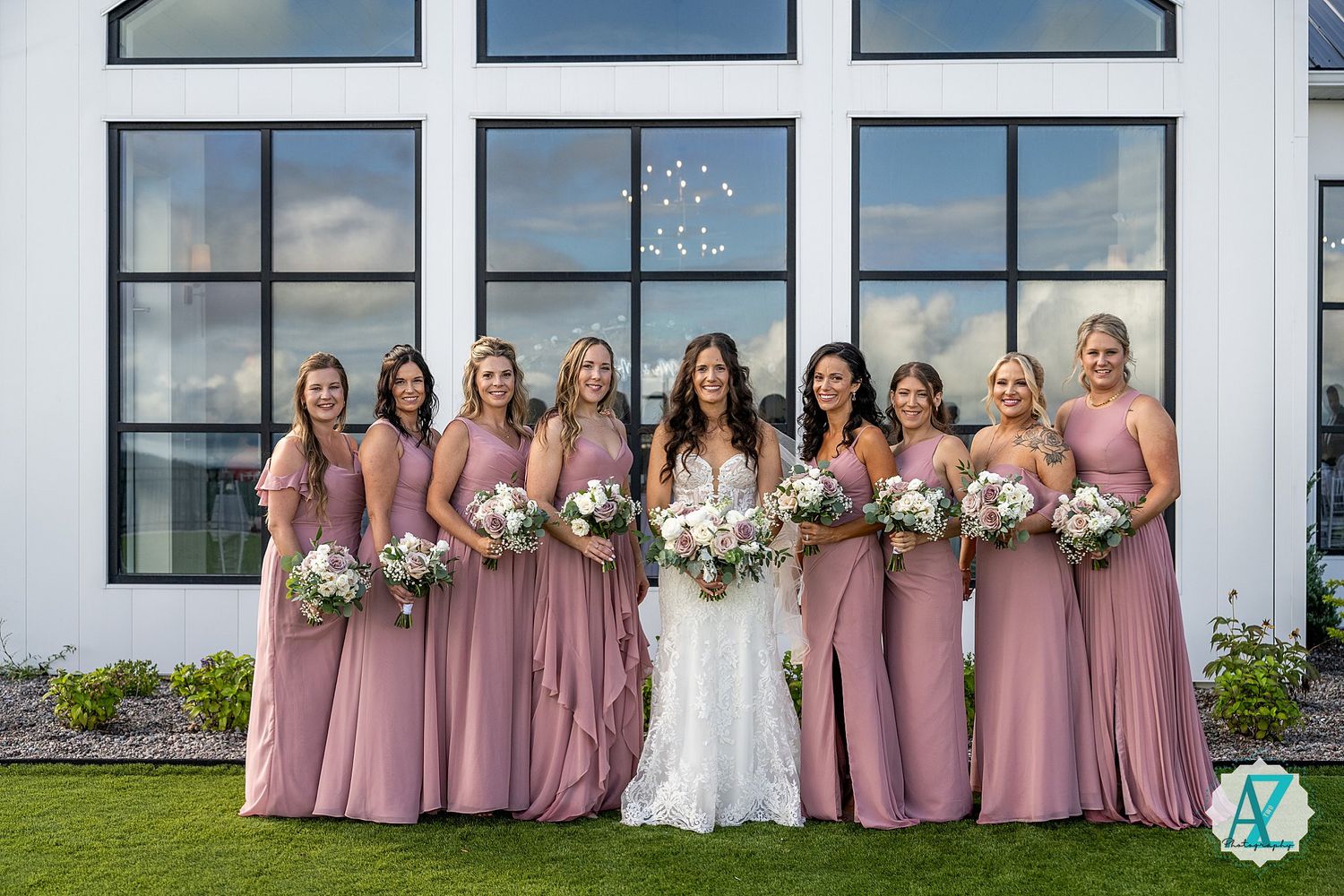 Bridesmaids in dusty rose dresses posed in front of modern building with large windows.