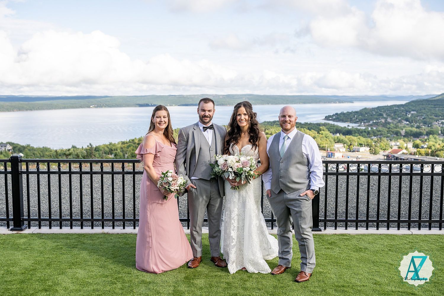Wedding party gathers on scenic lakeside terrace with mountain views in background.
