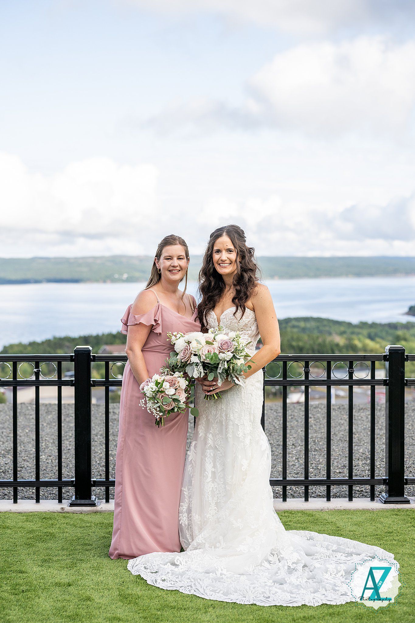A bridal party in pink and white dresses posing by a railing with waterfront views.