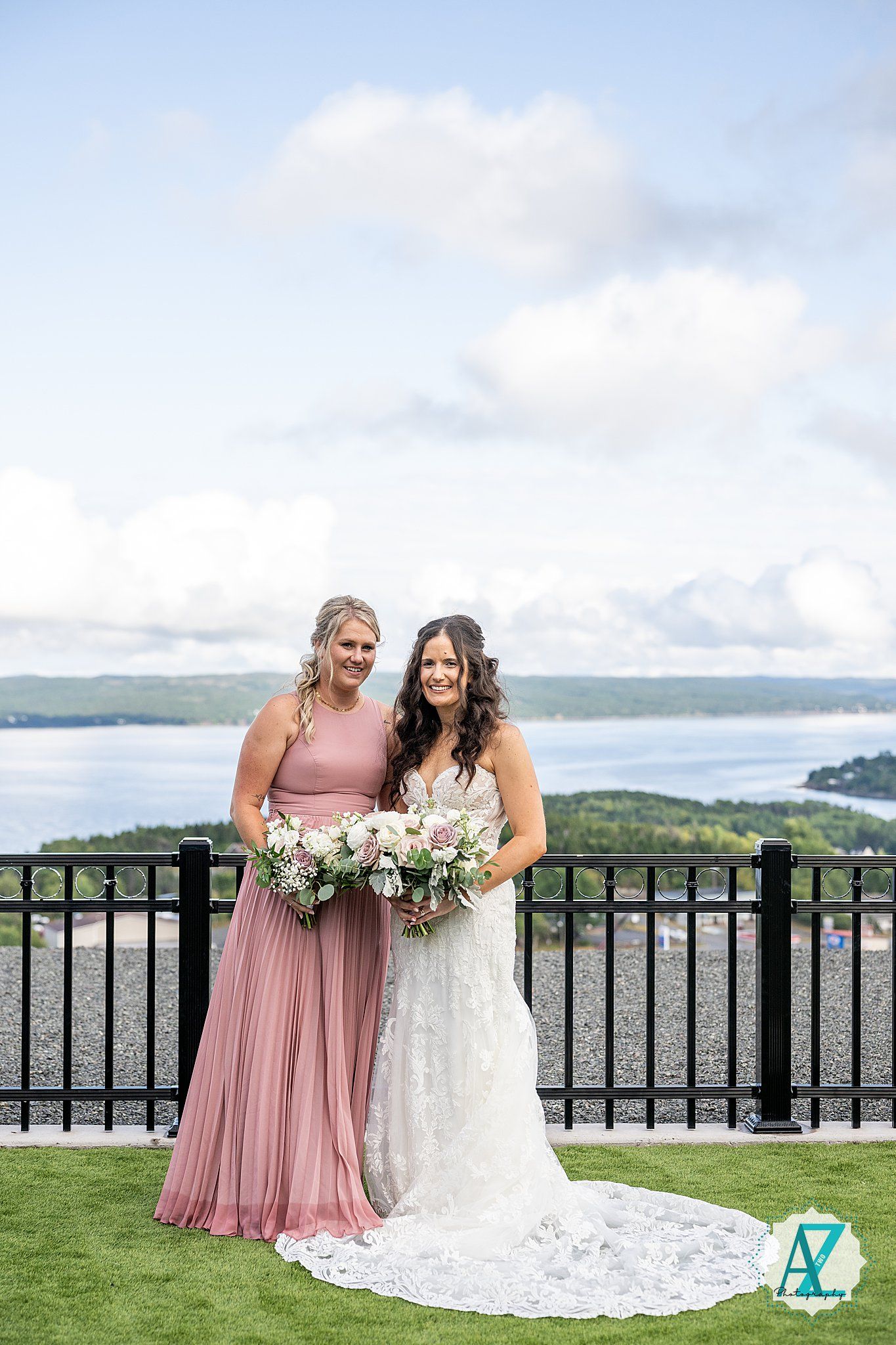 Wedding party stands together on a lush green lawn overlooking a beautiful waterfront vista on a cloudy day.
