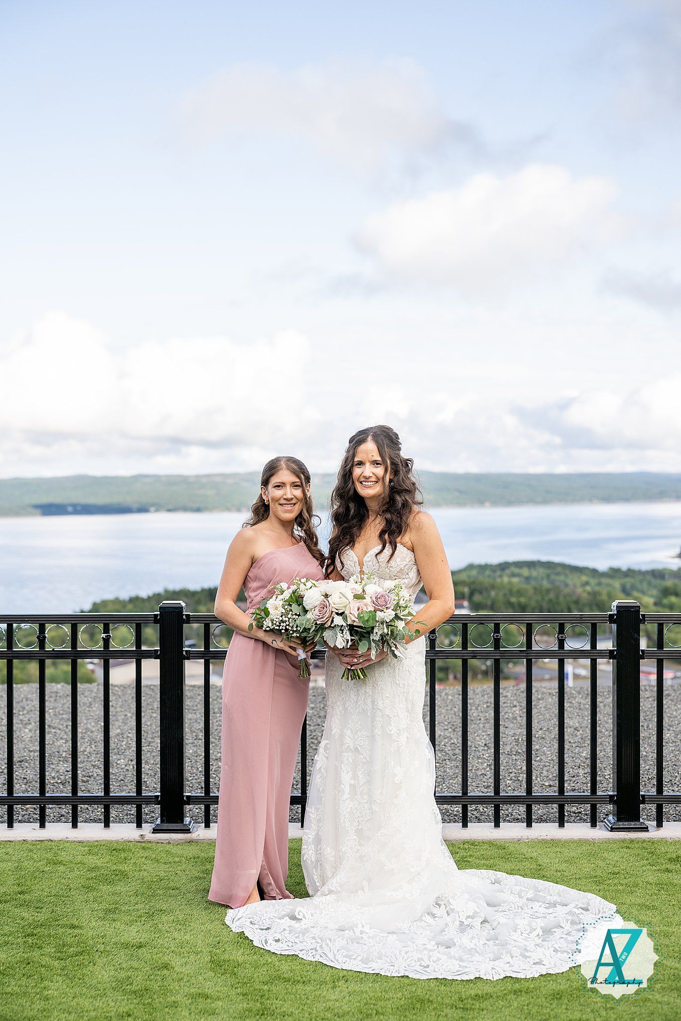 Wedding party members in pink and white dresses posing by a railing with scenic water views.