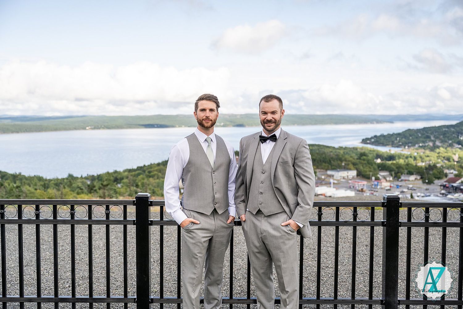 Groomsmen in grey suits and bowties stand together on panoramic outdoor terrace.