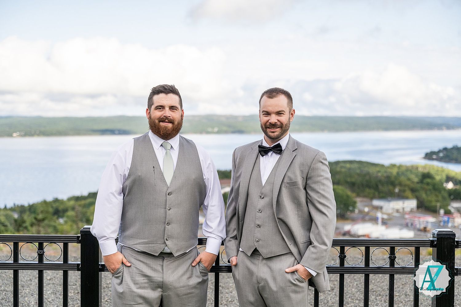 Groomsmen in light gray suits and vests pose against scenic waterfront backdrop during outdoor wedding celebration.