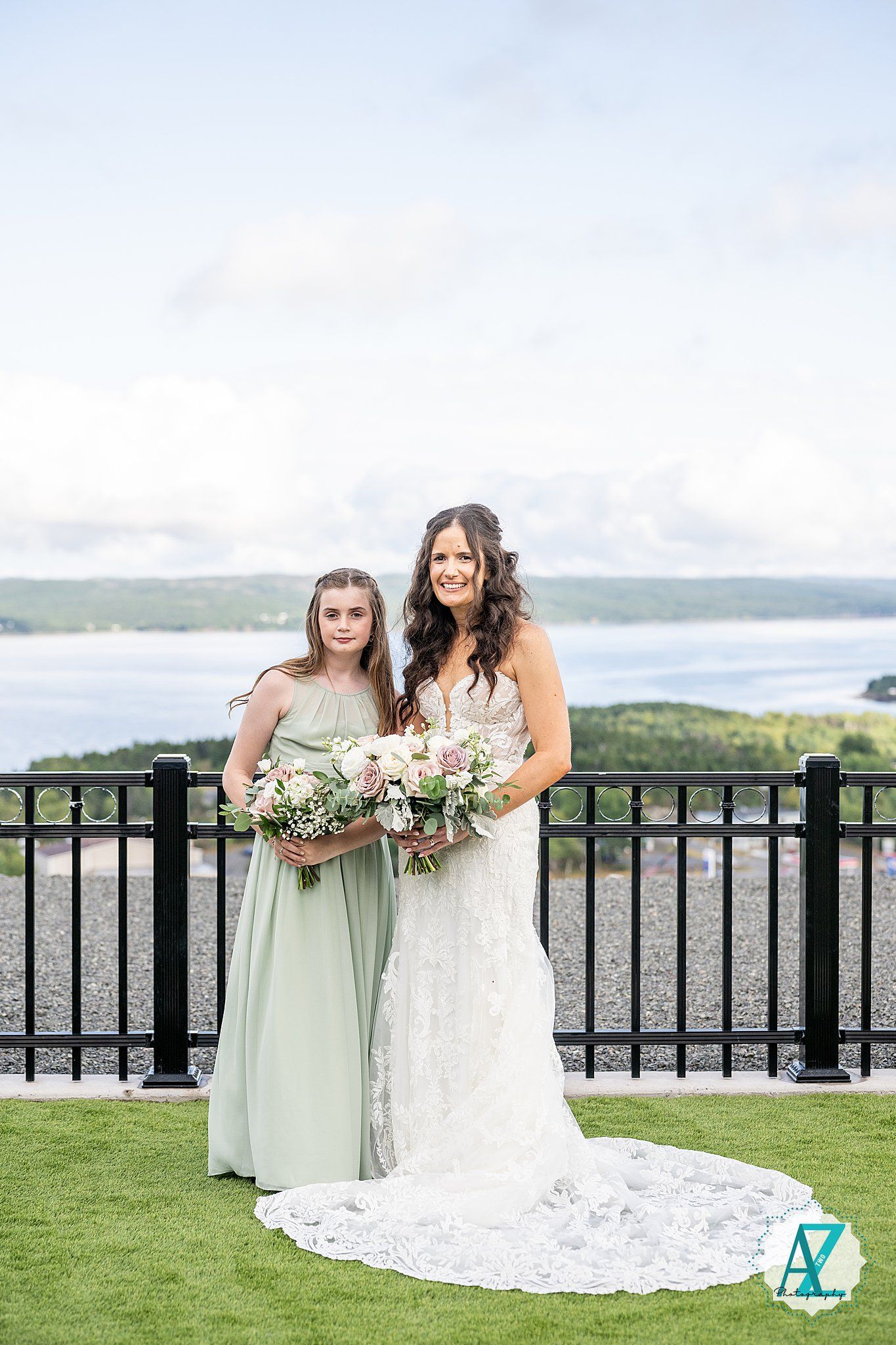 Bridesmaids in sage and white dresses share a moment on scenic outdoor terrace.