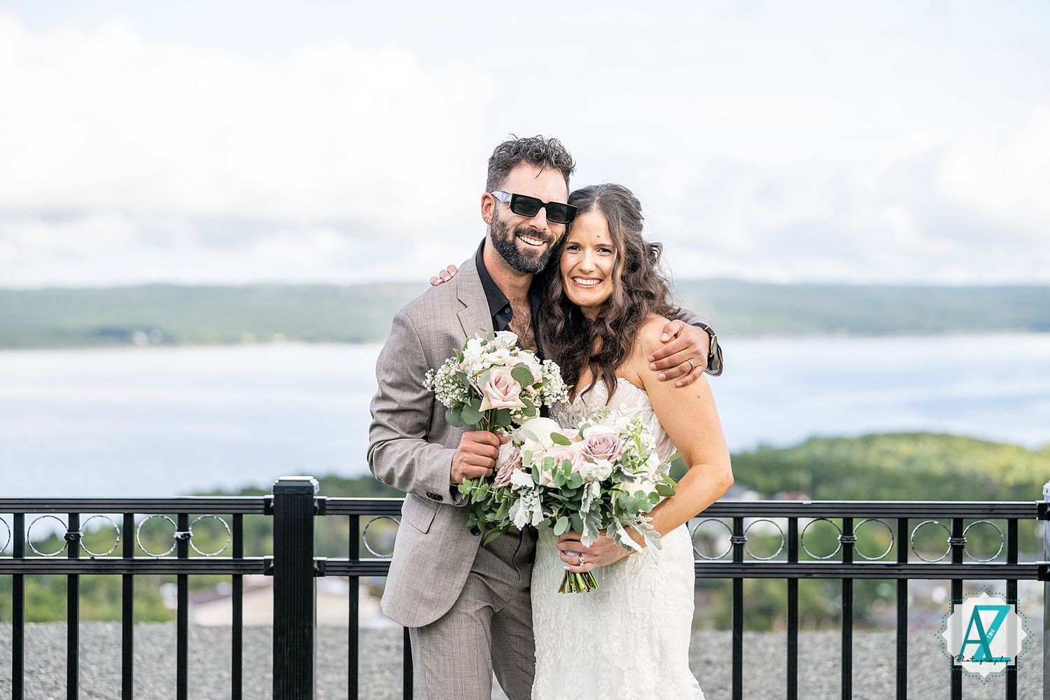 Wedding party poses together against backdrop of scenic water and rolling hills.