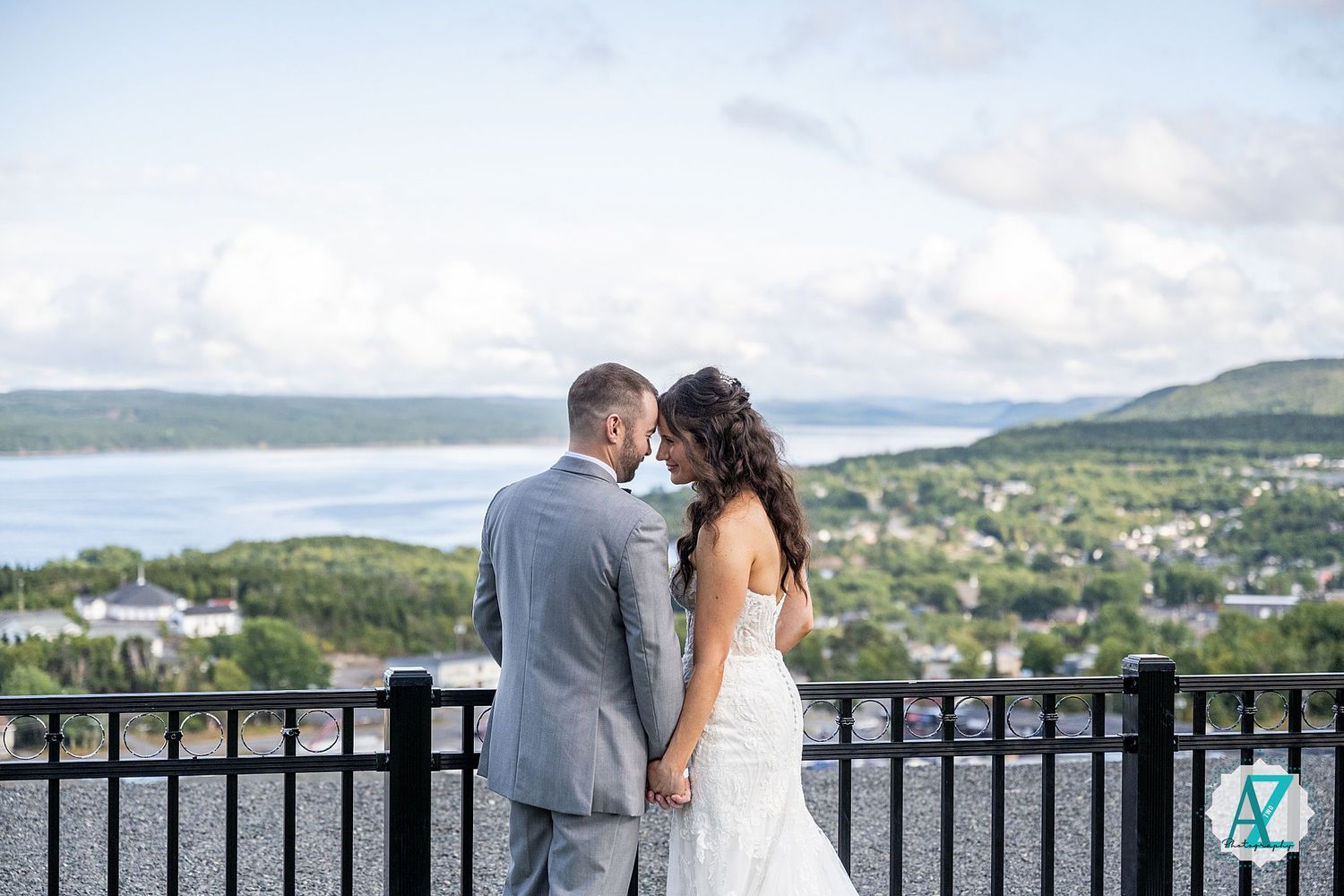 Wedding couple shares intimate moment on balcony overlooking scenic waterfront landscape.
