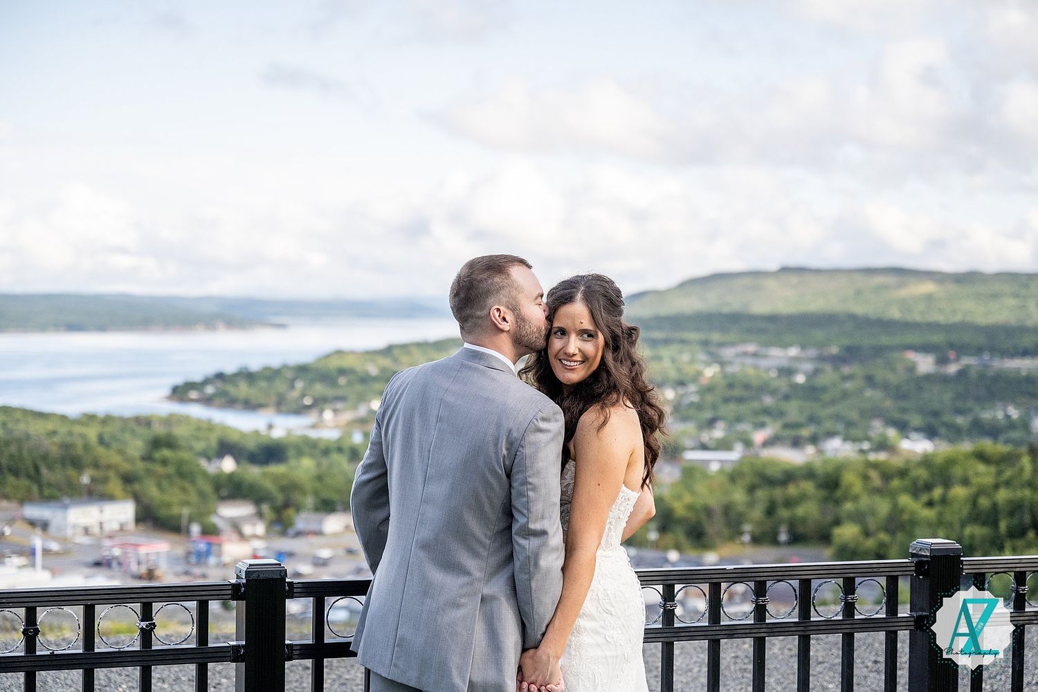 Couple celebrates their wedding day on scenic overlook with water and hills in background.