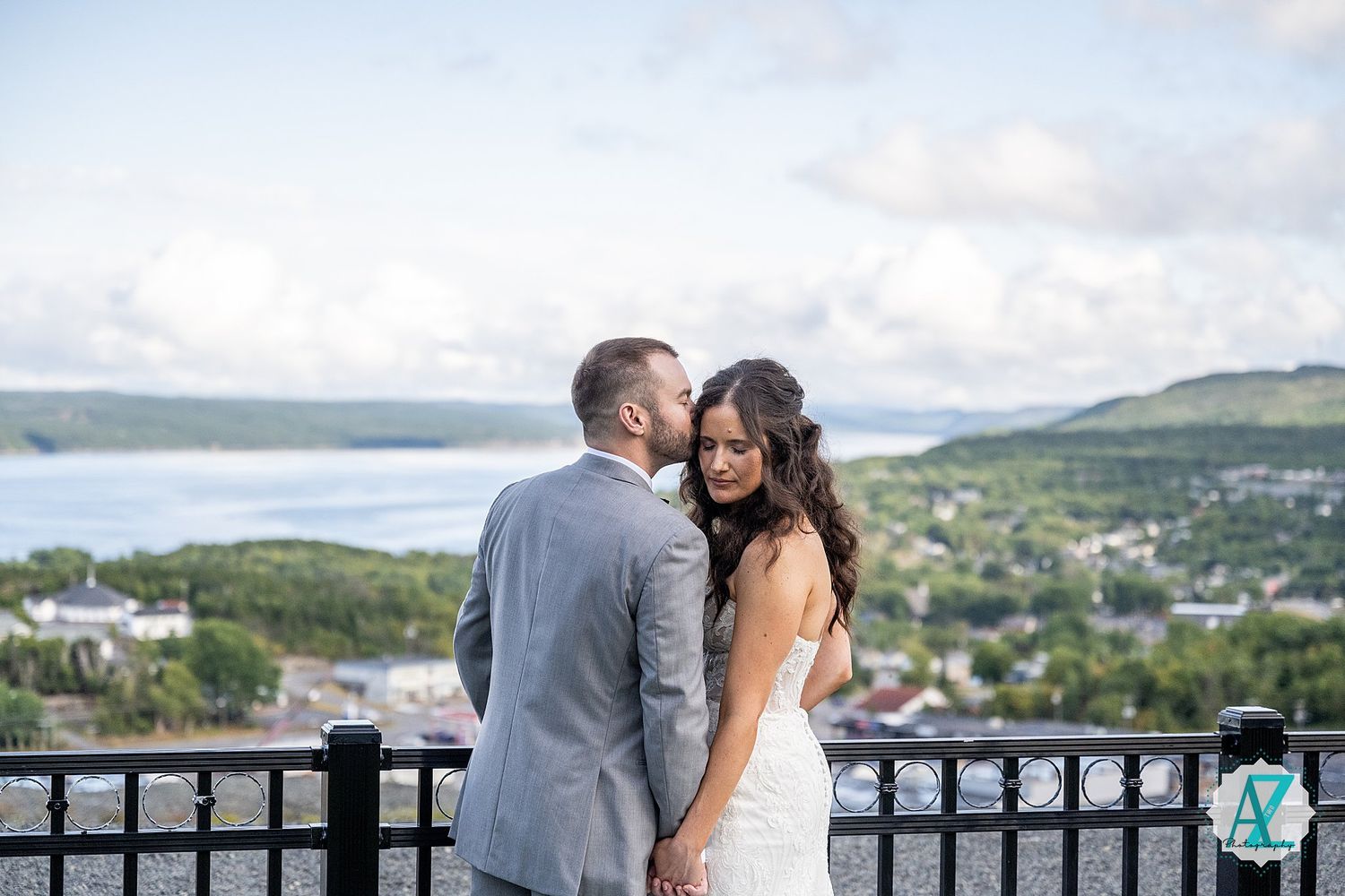 Wedding couple poses on outdoor terrace with scenic coastal landscape behind them.