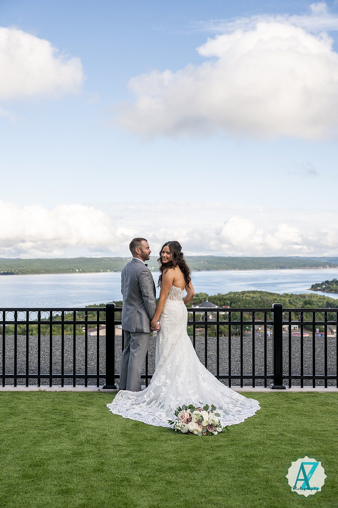 Couple shares intimate moment on scenic outdoor terrace with water views and flowing wedding dress.