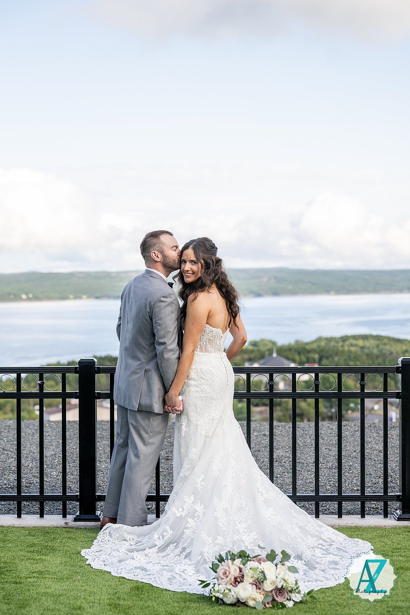 Romantic wedding portrait of couple embracing on terrace overlooking scenic water landscape.