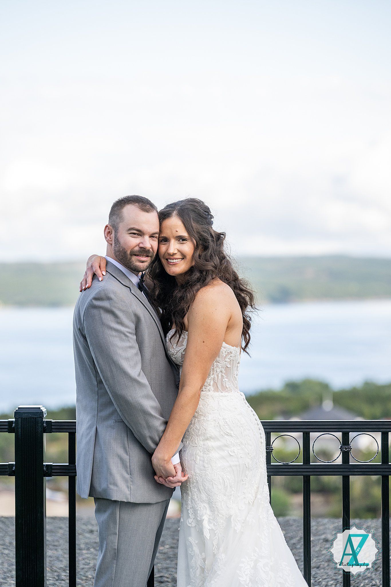 A couple in wedding attire share romantic moments along a balcony railing overlooking a scenic outdoor view.