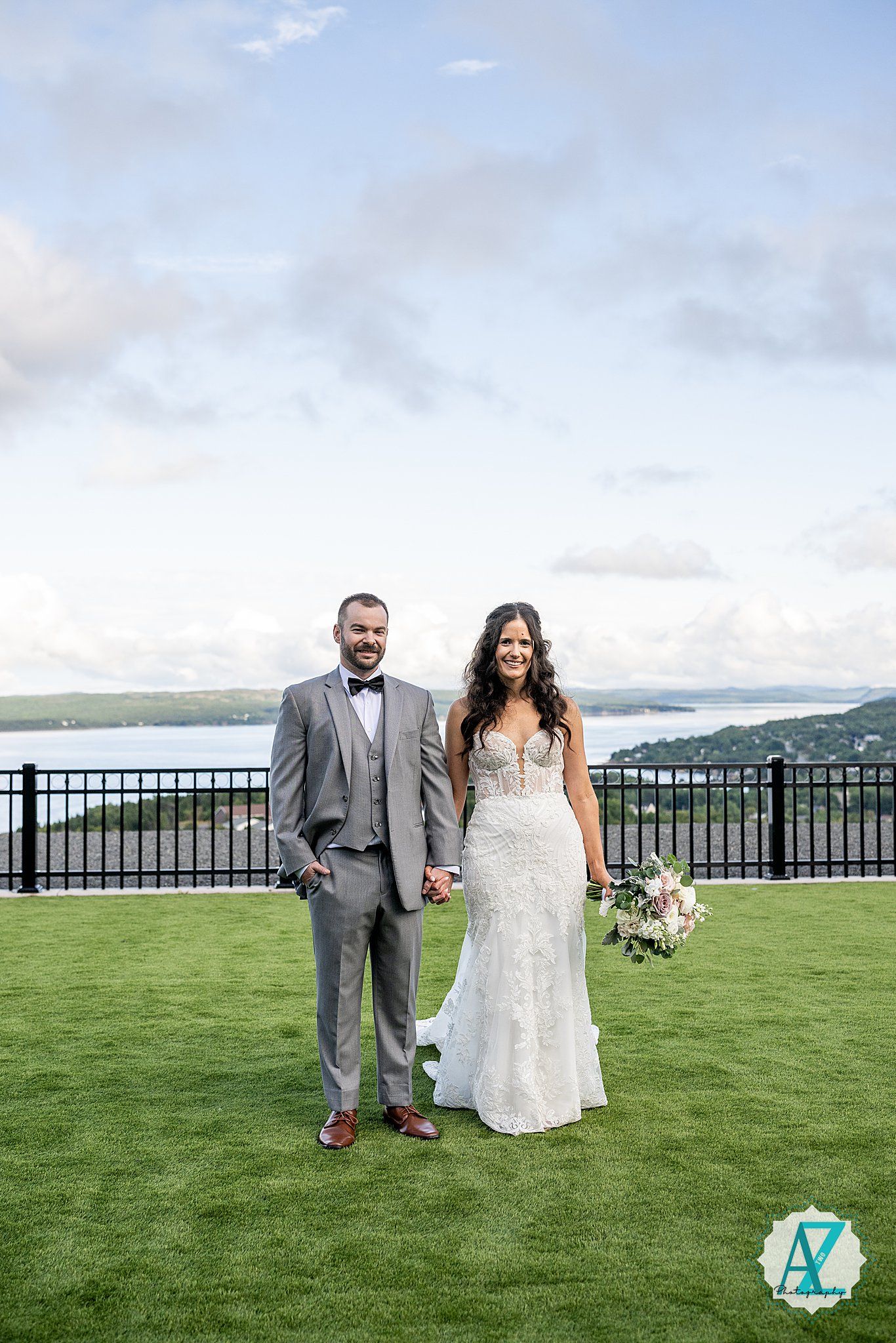 A couple in wedding attire walks on a lush green lawn overlooking a scenic mountain view.