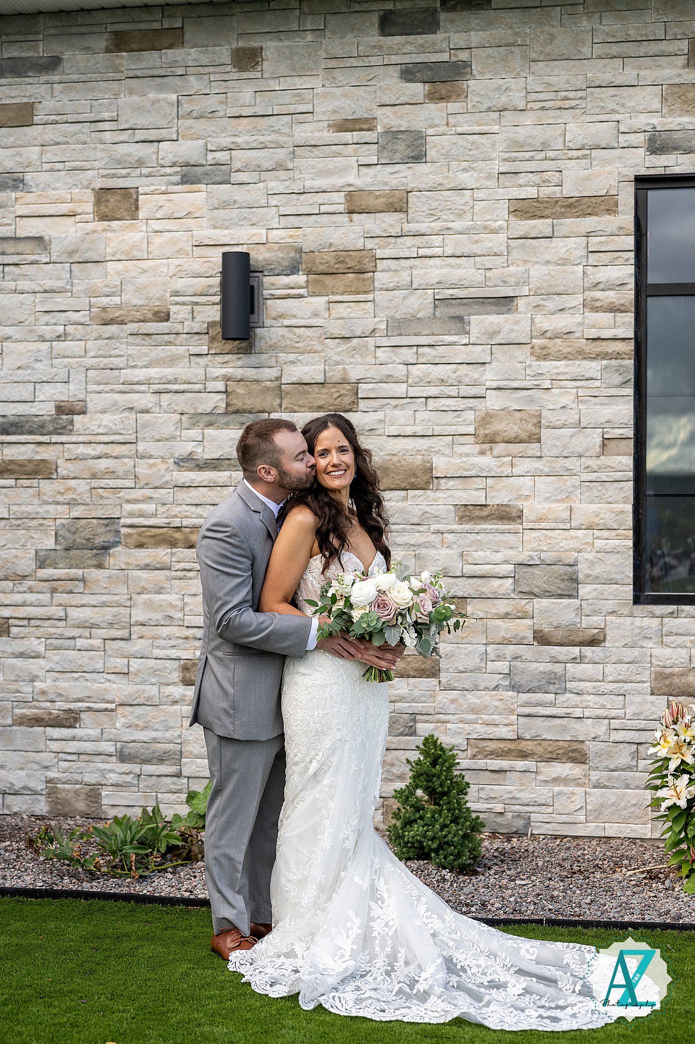 A couple shares an intimate moment against a stone wall backdrop during their wedding photoshoot.