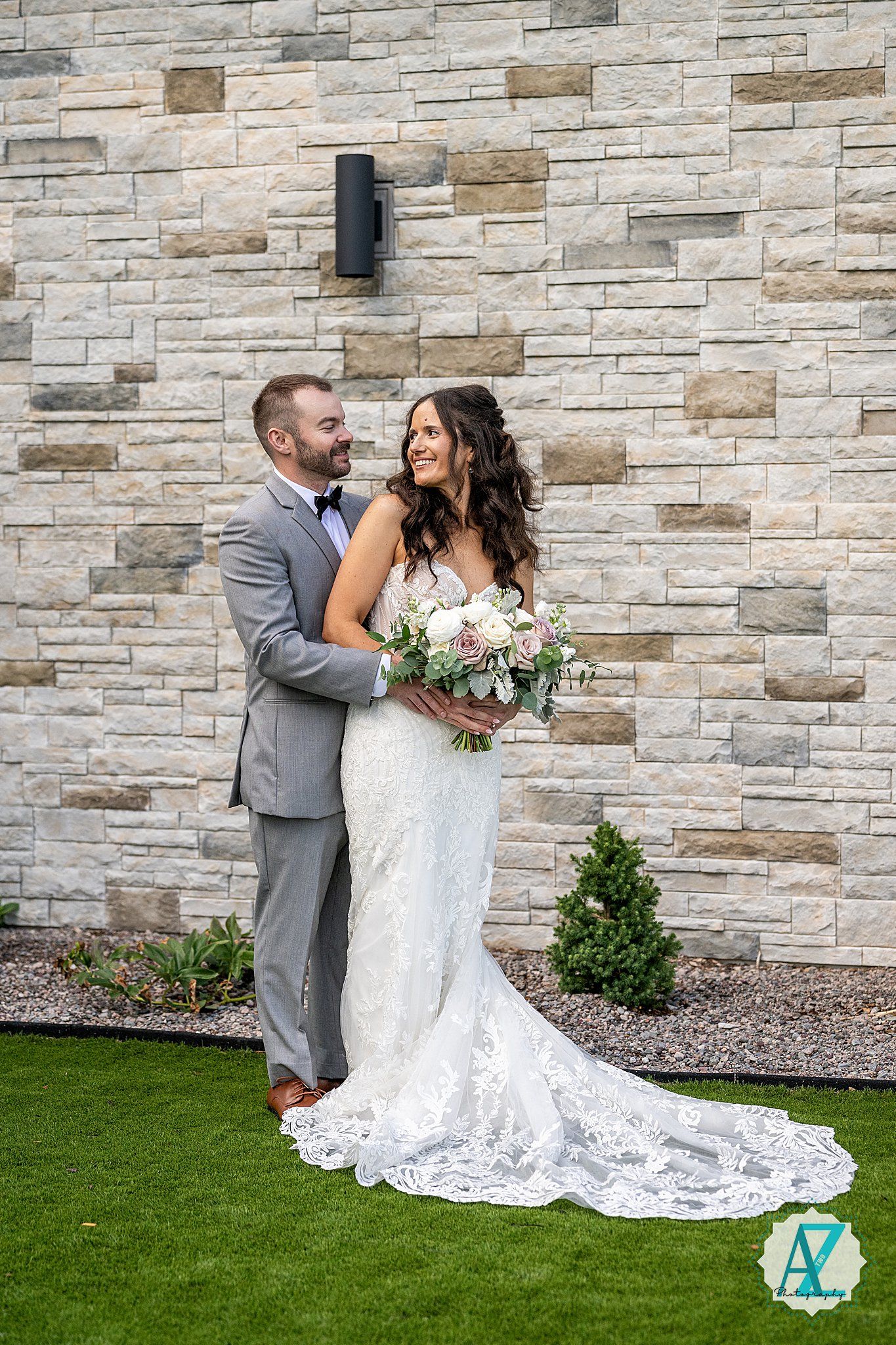 Wedding couple shares romantic moments against a stone wall backdrop in their formal attire.