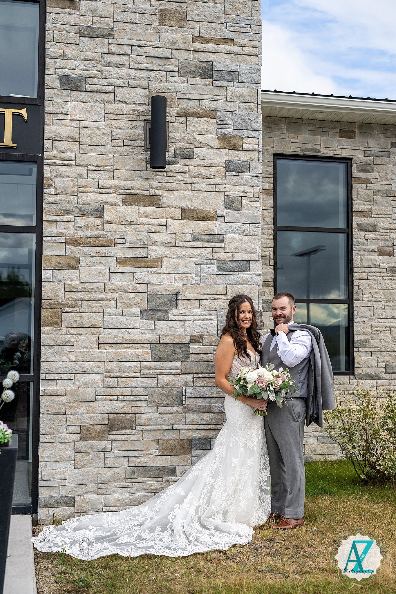 A couple poses against a stone wall exterior with flowing white wedding dress and gray suit.
