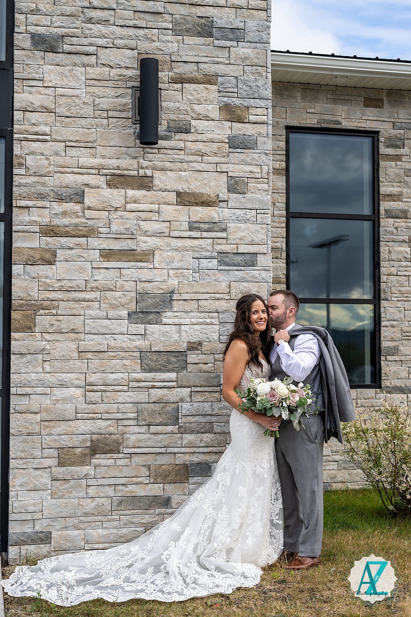 A couple shares a romantic moment against a modern stone building facade.