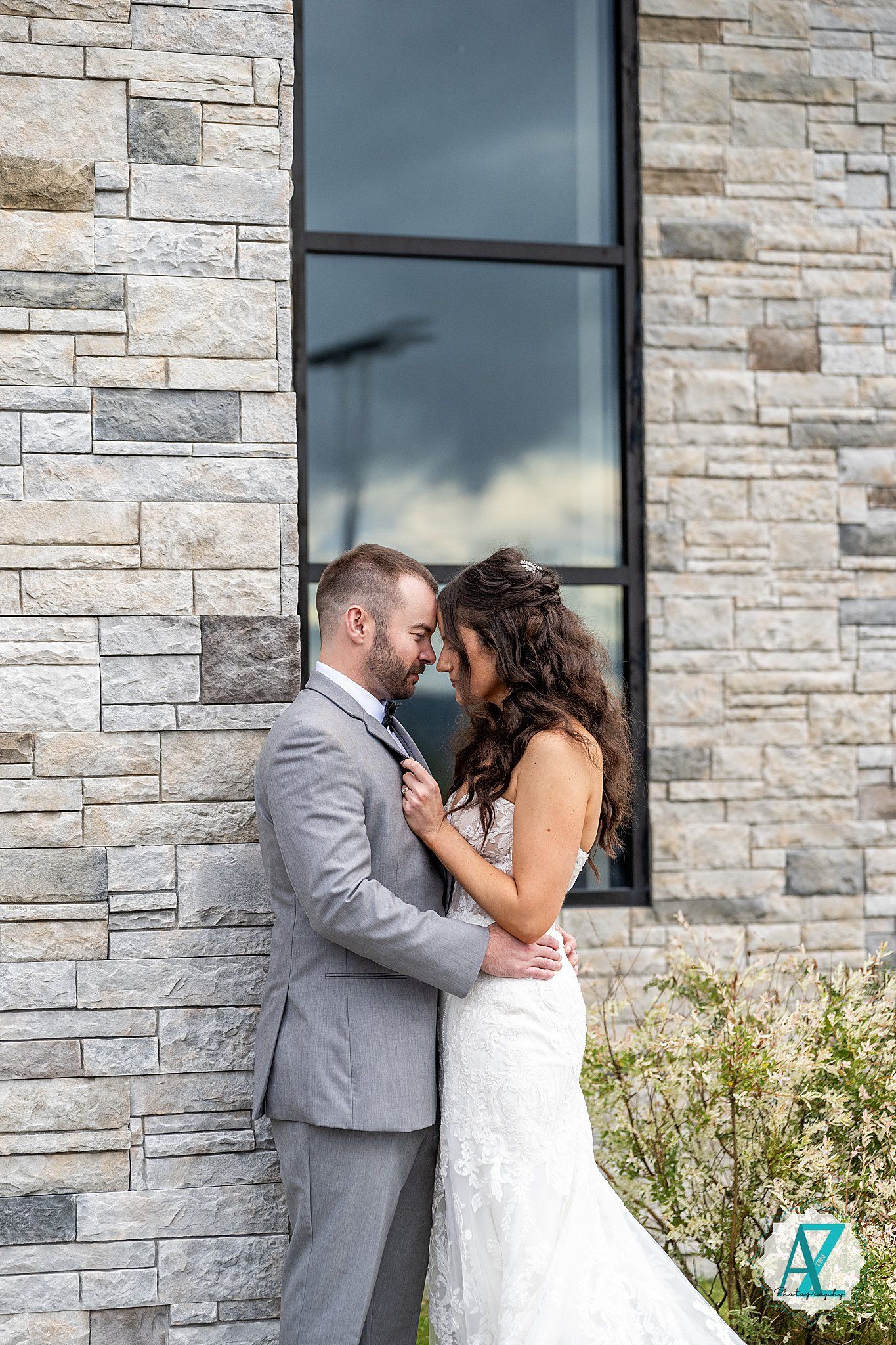 Newlyweds share intimate moments against a modern stone wall exterior of a building.