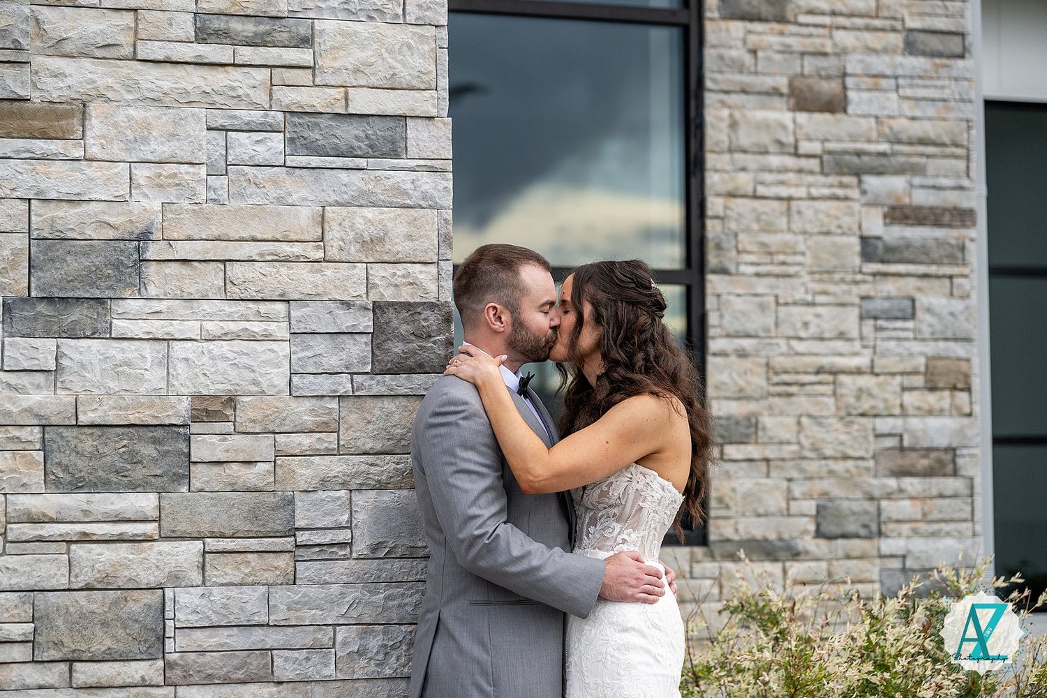 A romantic moment captured outside a modern stone building with elegant lighting and architectural details.