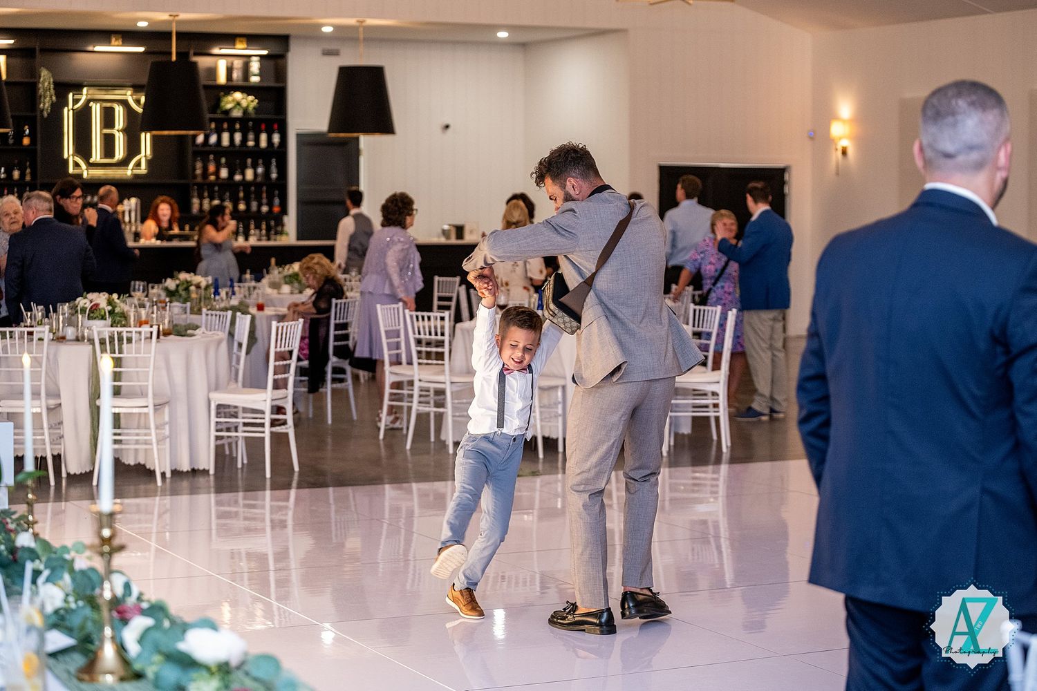 Modern white reception space with minimalist decor and groups gathering near a bar area.