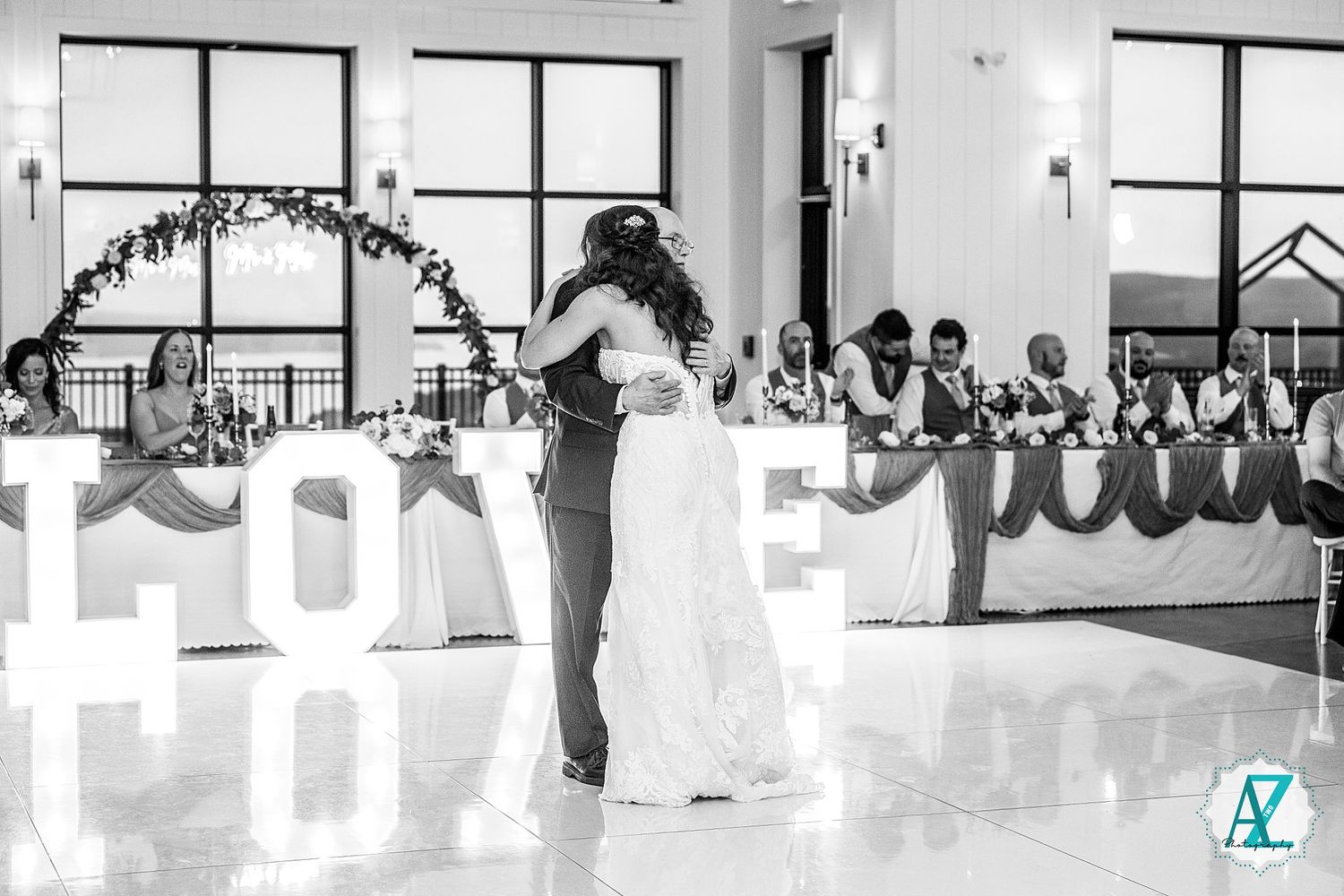 Black and white panoramic shot of a spacious wedding venue with large windows and hanging lights.