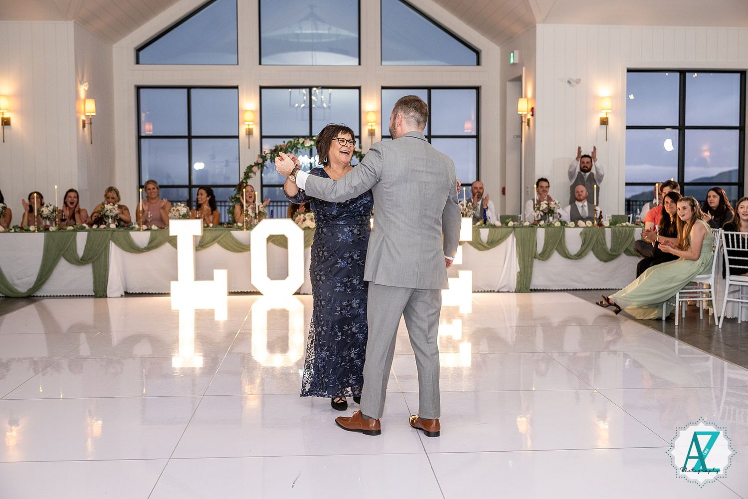 A reception dance scene with illuminated LOVE letters glowing in an elegant white venue with vaulted windows.