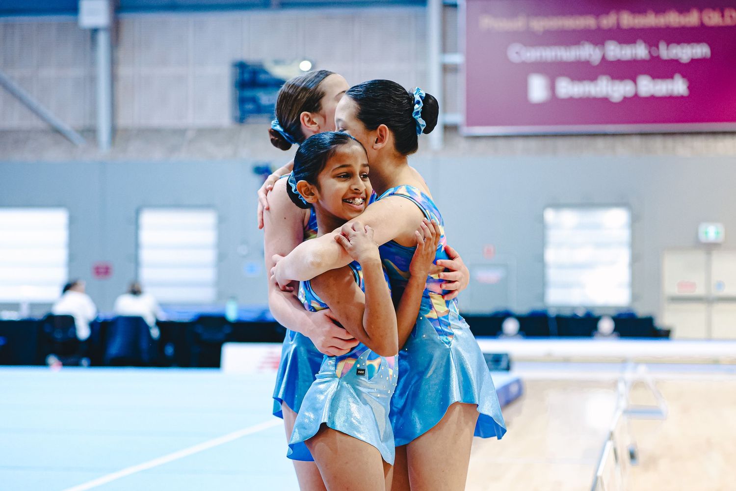 Competitive dancers wearing blue costumes embrace emotionally during a performance on stage.