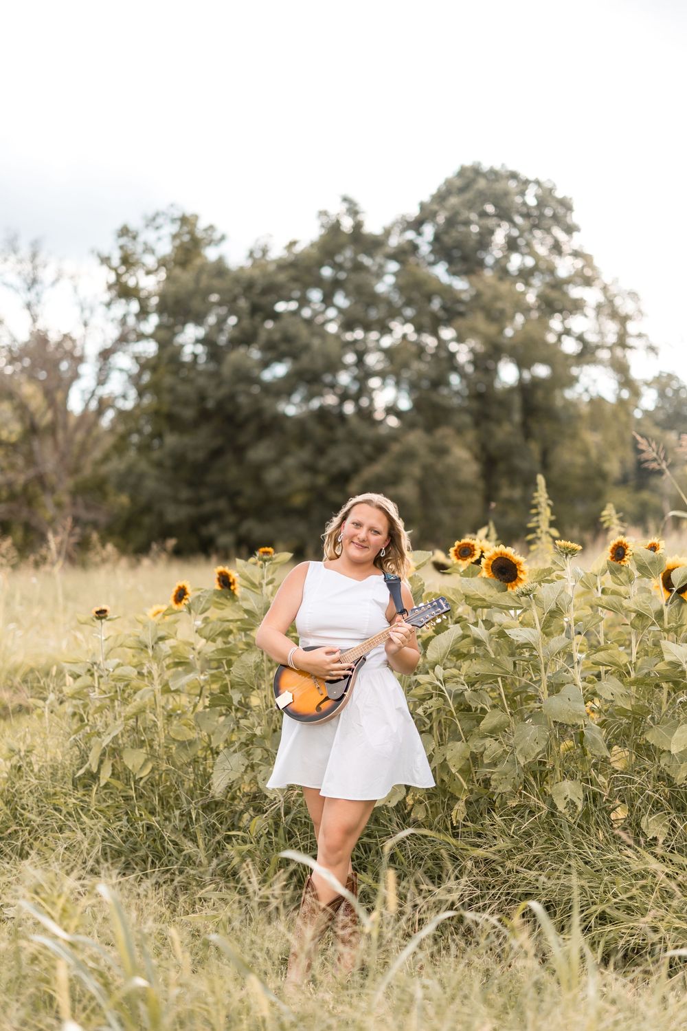 Woman in white dress poses gracefully in a blooming sunflower field at sunset.