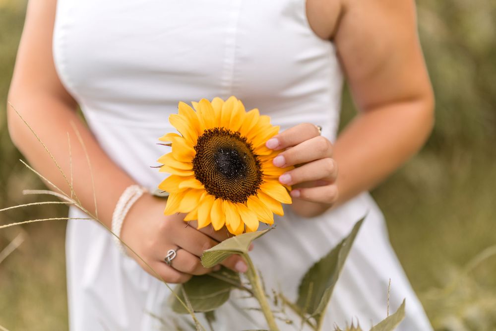 A person in white holding bright yellow sunflowers against a natural outdoor background.