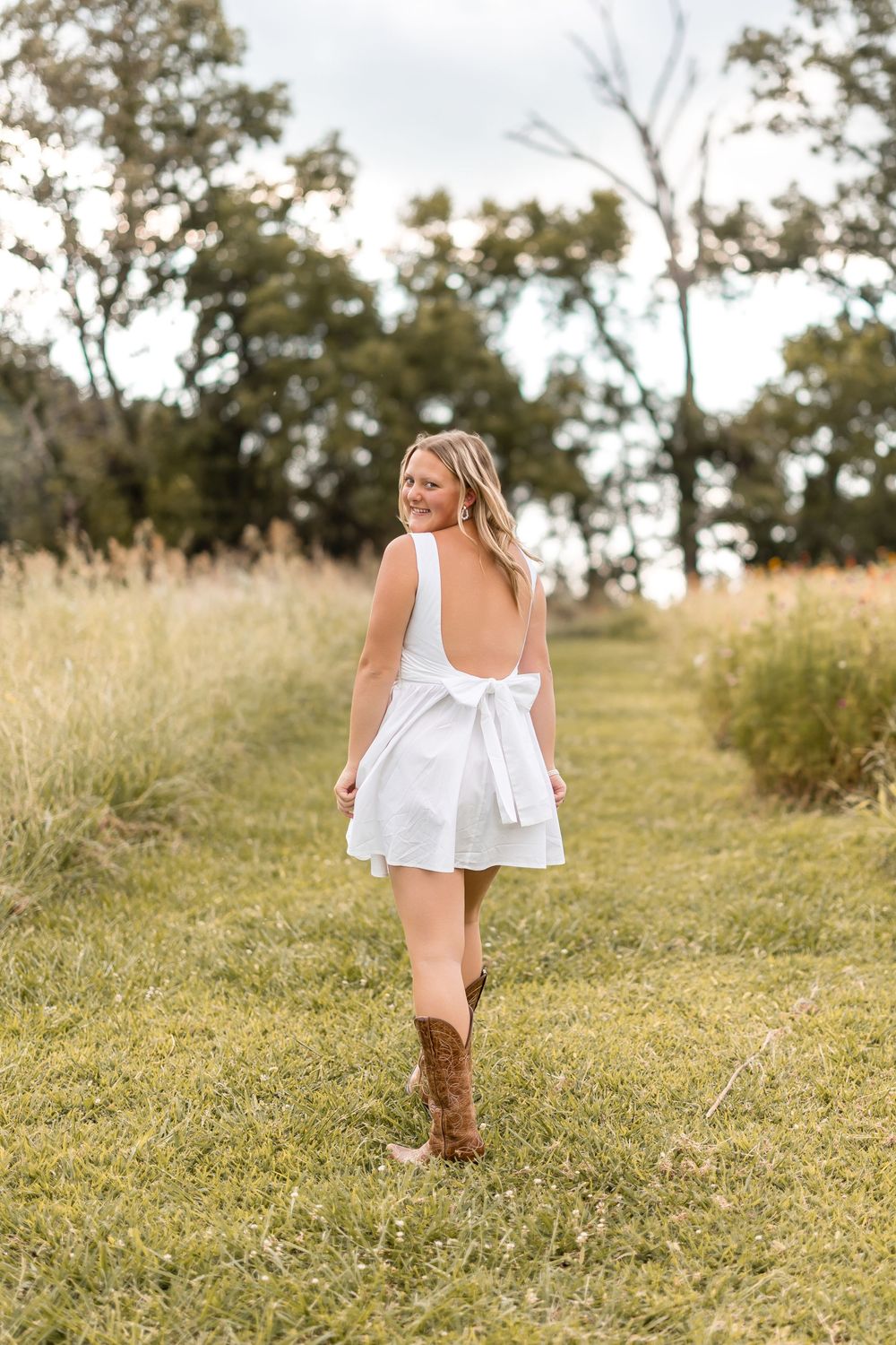 Young child in white dress and boots walking through sunny meadow.