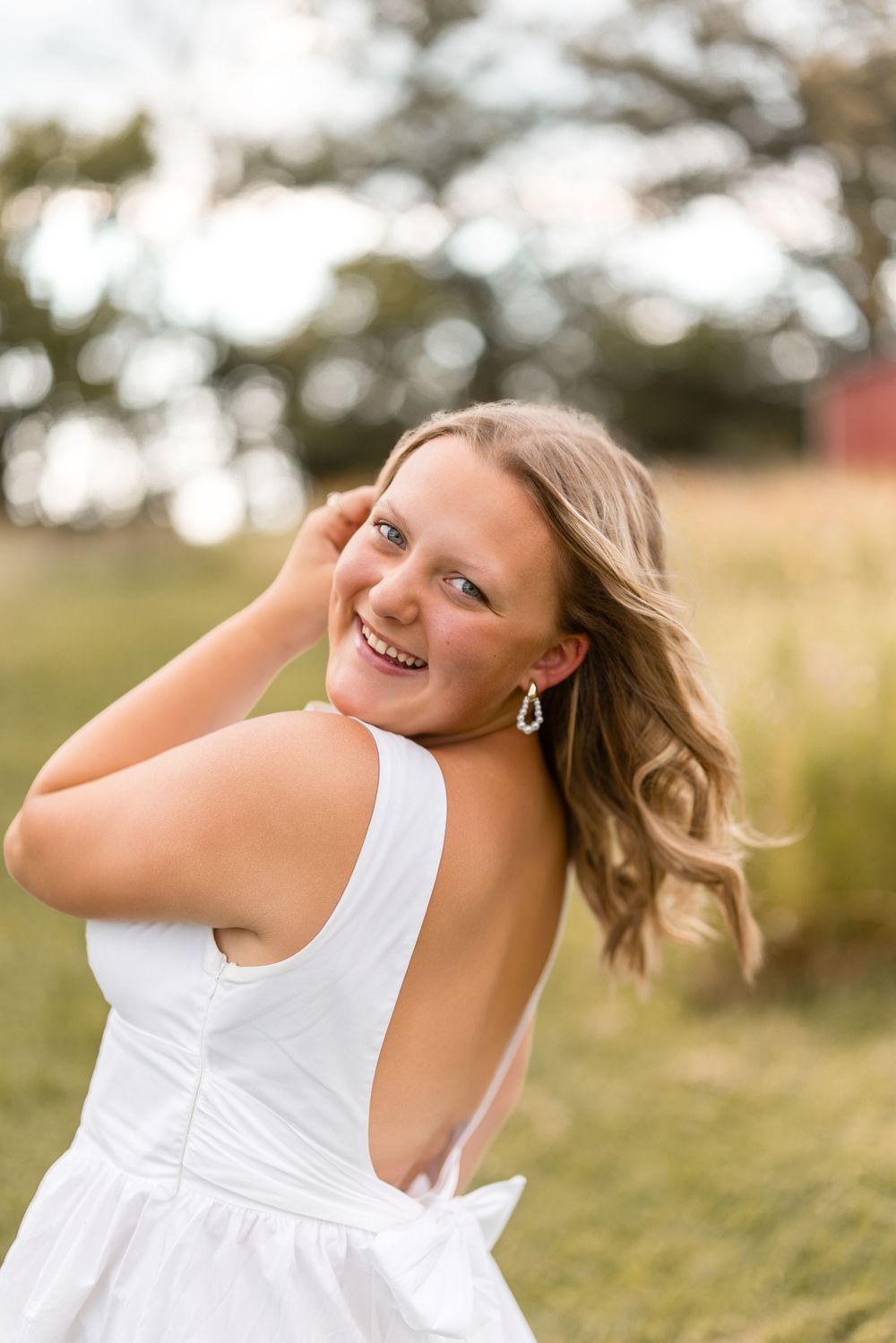 Woman in white summer dress twirls playfully in a sunny meadow with golden grass and trees in background.