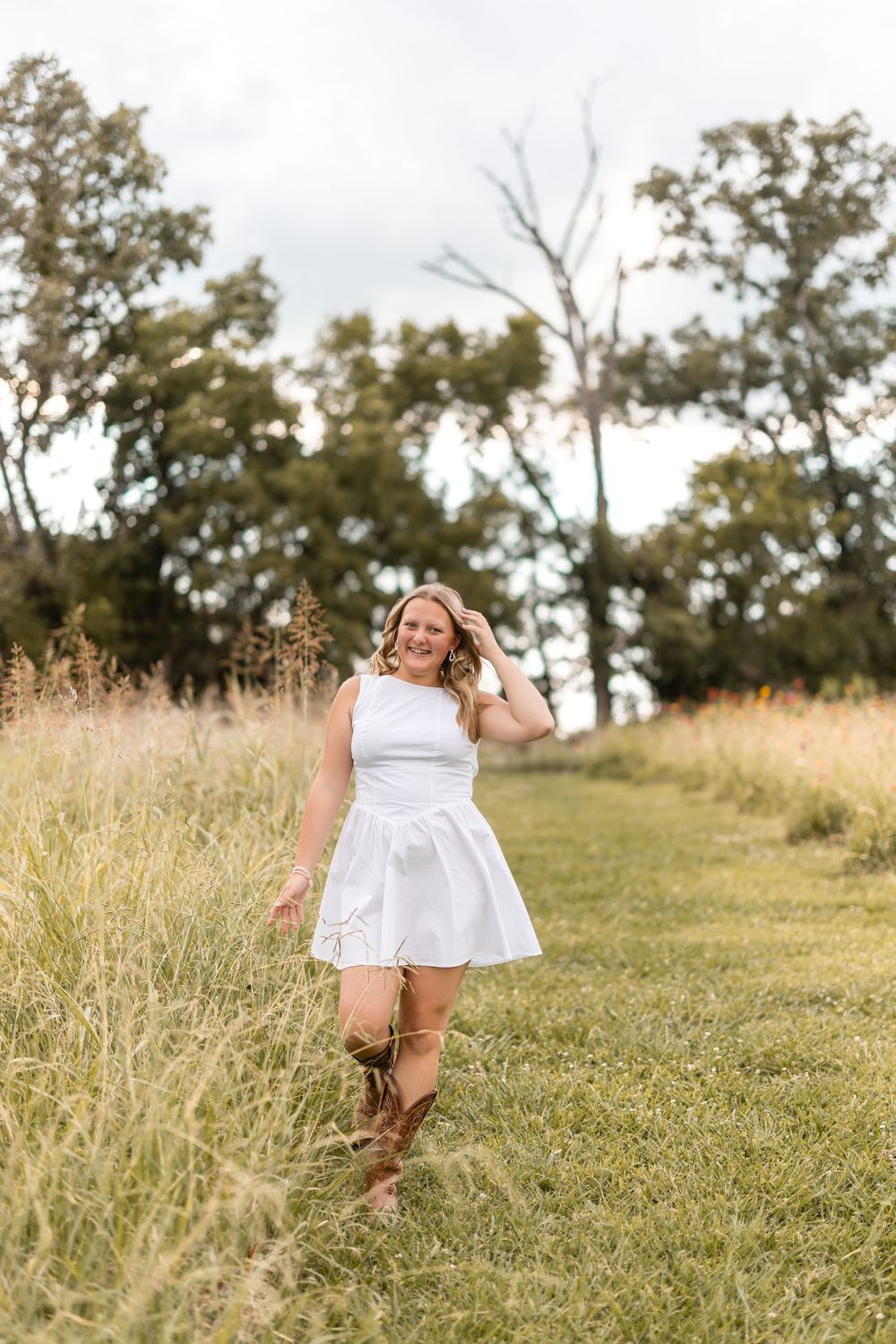 Dancing figure in white dress moves gracefully through a grassy hillside on a warm summer afternoon.