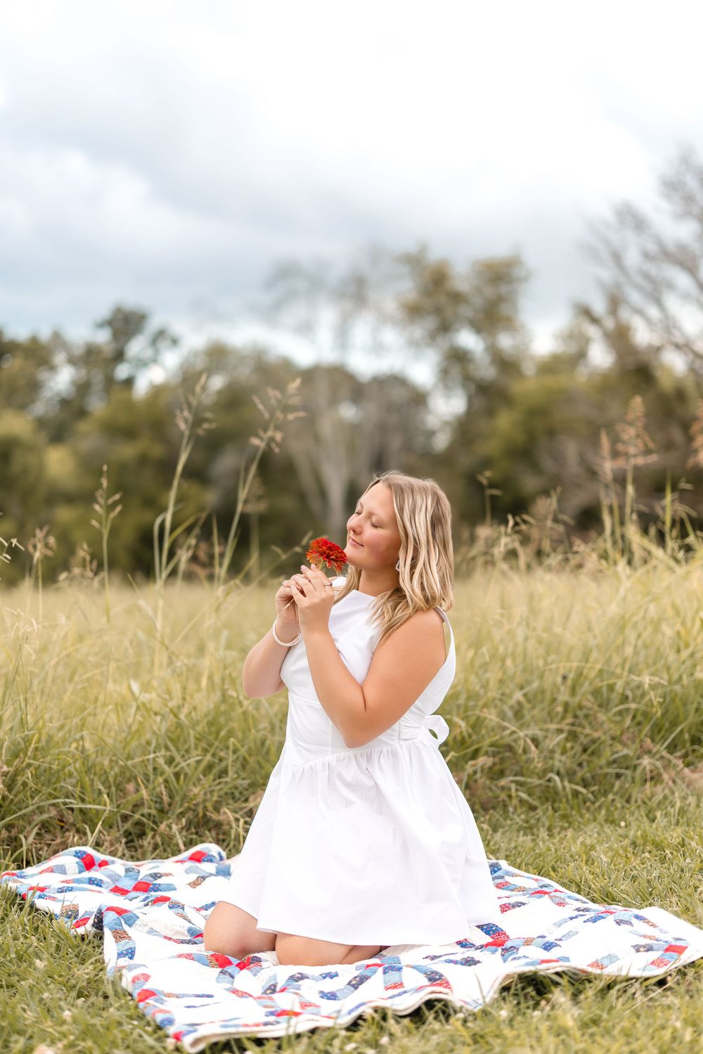 Woman in white dress relaxing on a colorful blanket in a sunny meadow.