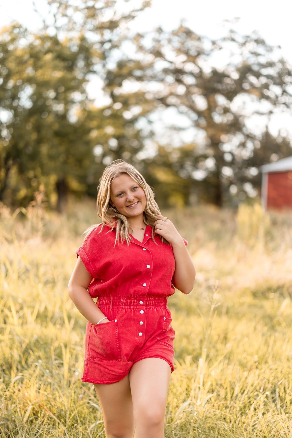 Woman in red romper posing playfully in a golden field during sunset.